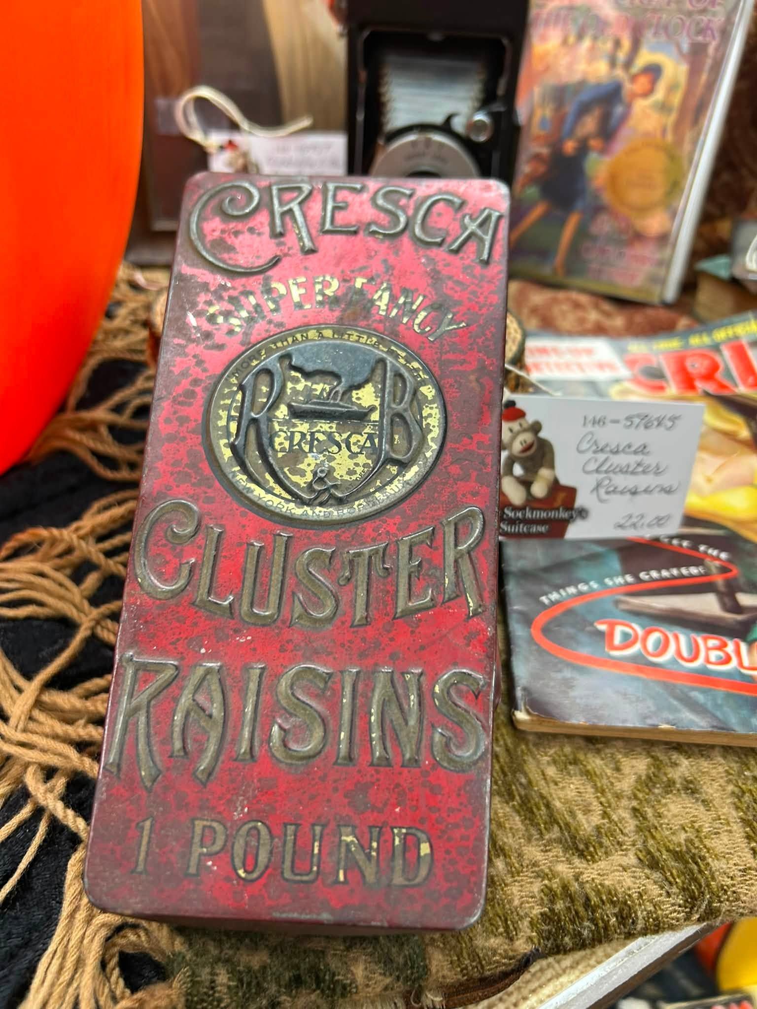 Vintage red tin sign reading “Cresca Cluster Raisins 1 Pound” at a market display.