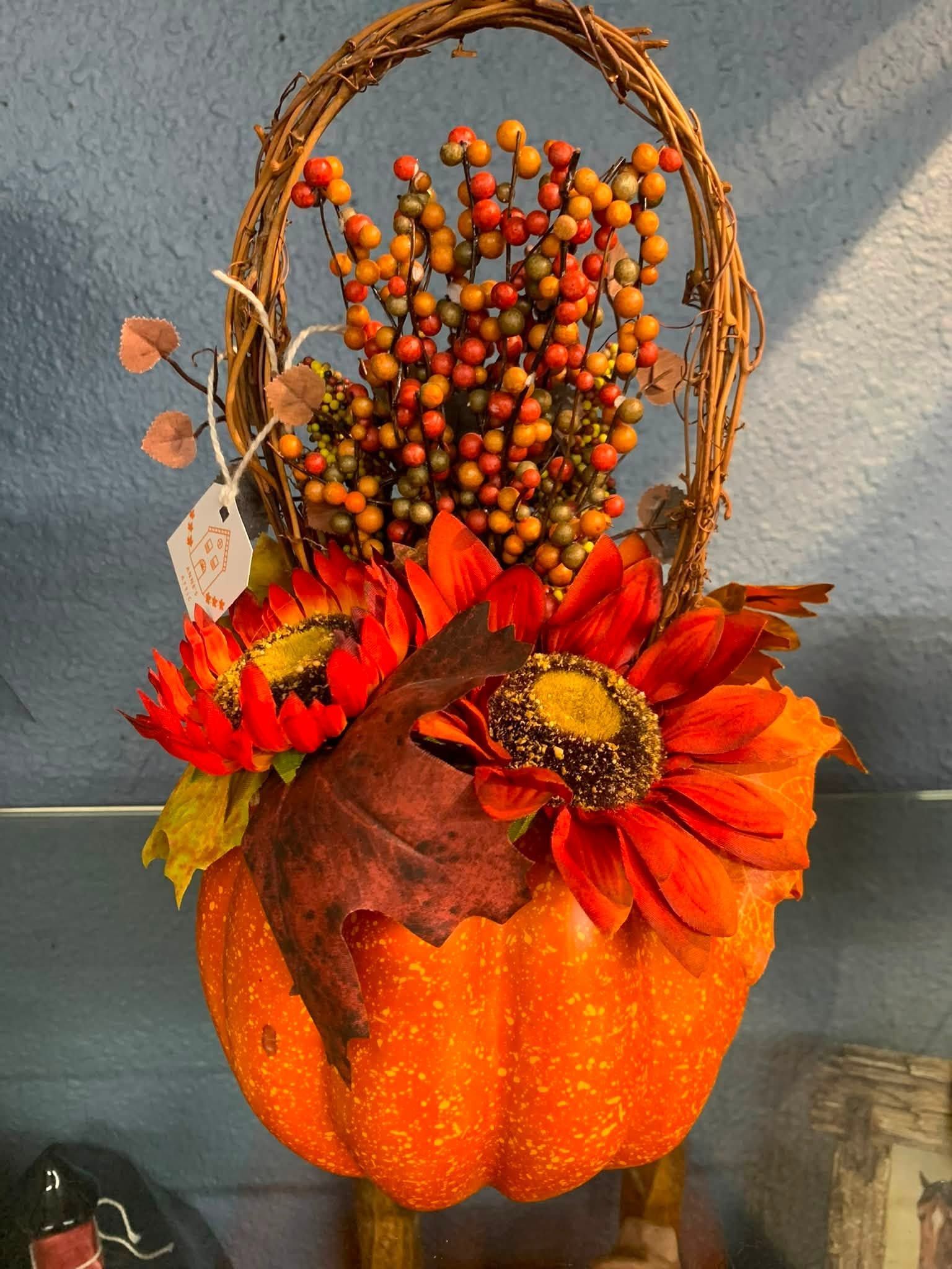 Fall pumpkin basket with red flowers, berries, and a woven handle on a tabletop