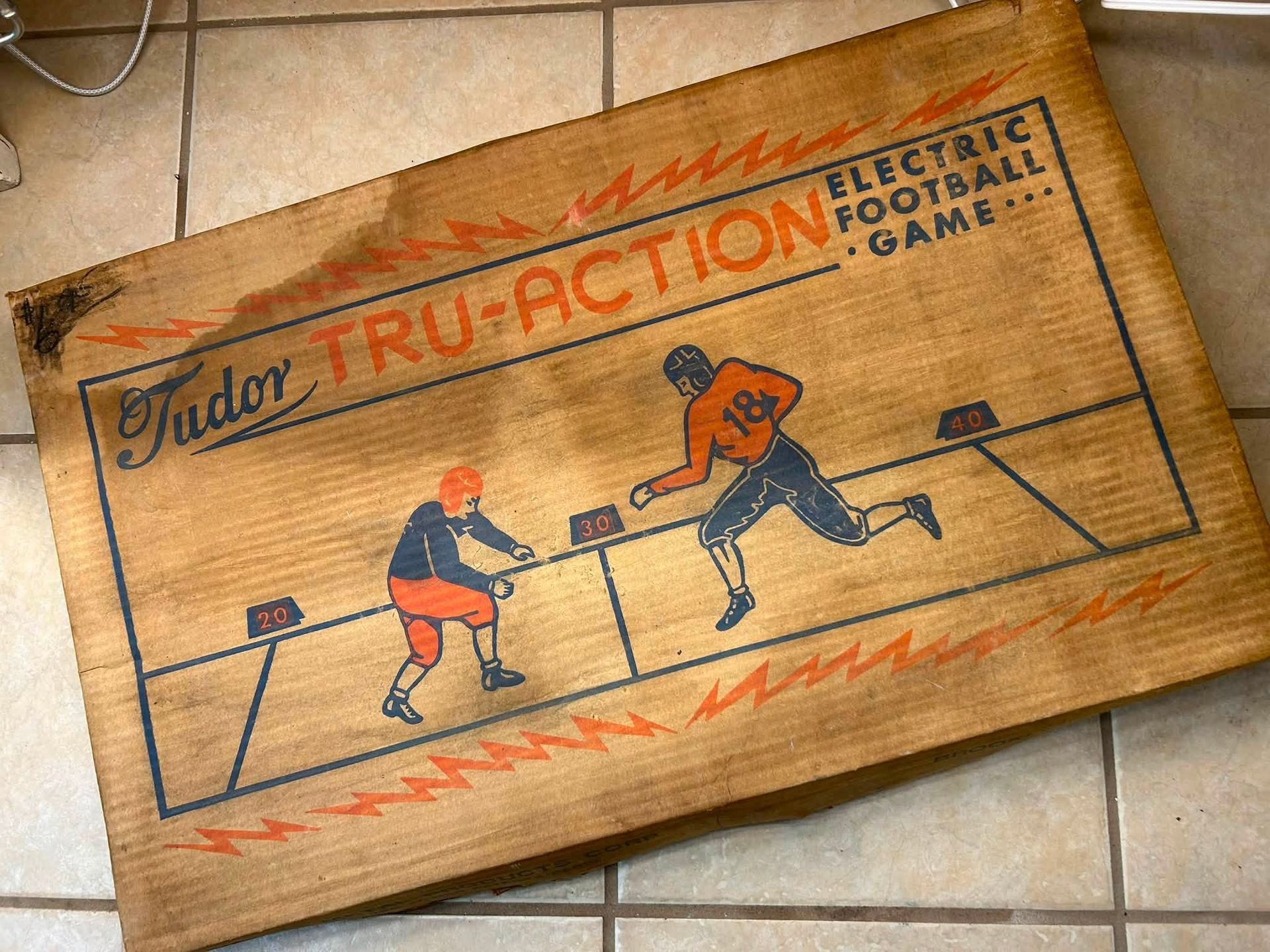 Vintage wooden table football game board on tiled floor, with orange and black players in action.