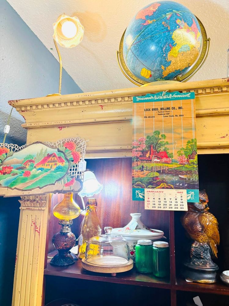 Decorated home altar with globe, lamp, framed calendars, and offerings on shelves