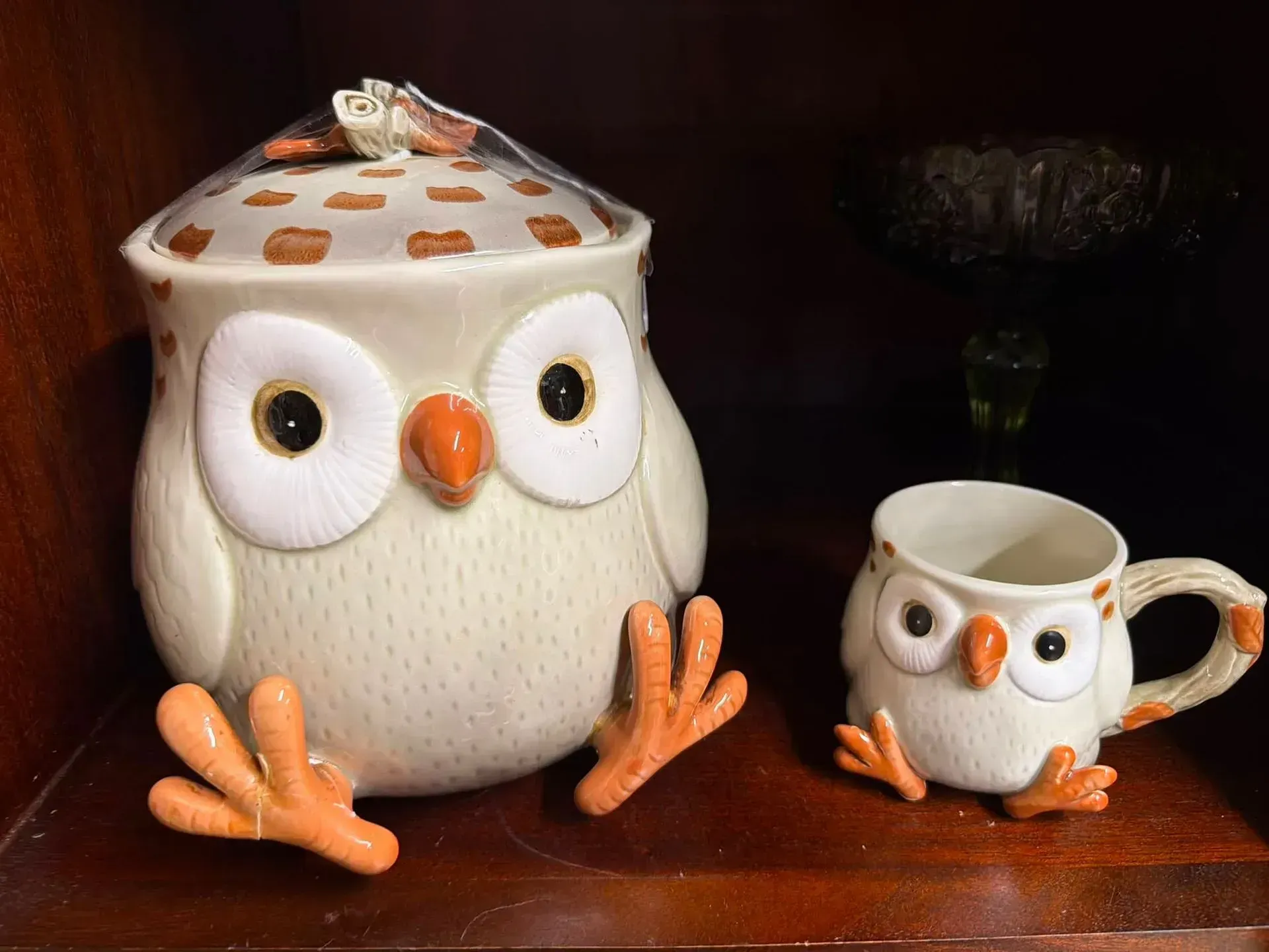 Large white owl figurine with lid beside a tiny owl-shaped mug on a dark wooden shelf