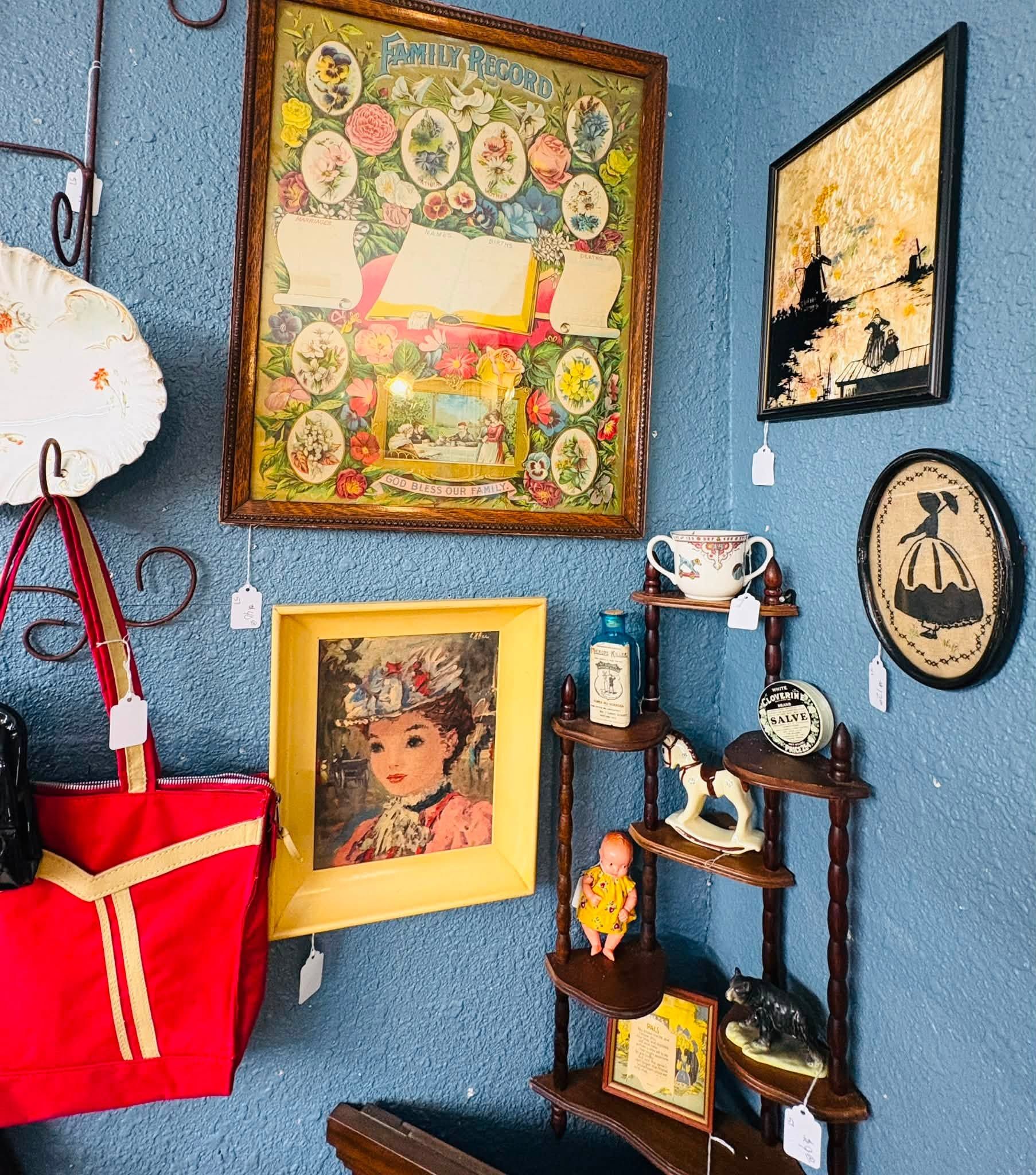 Blue wall with framed art, a red tote, and a small corner shelf with figurines and decor.