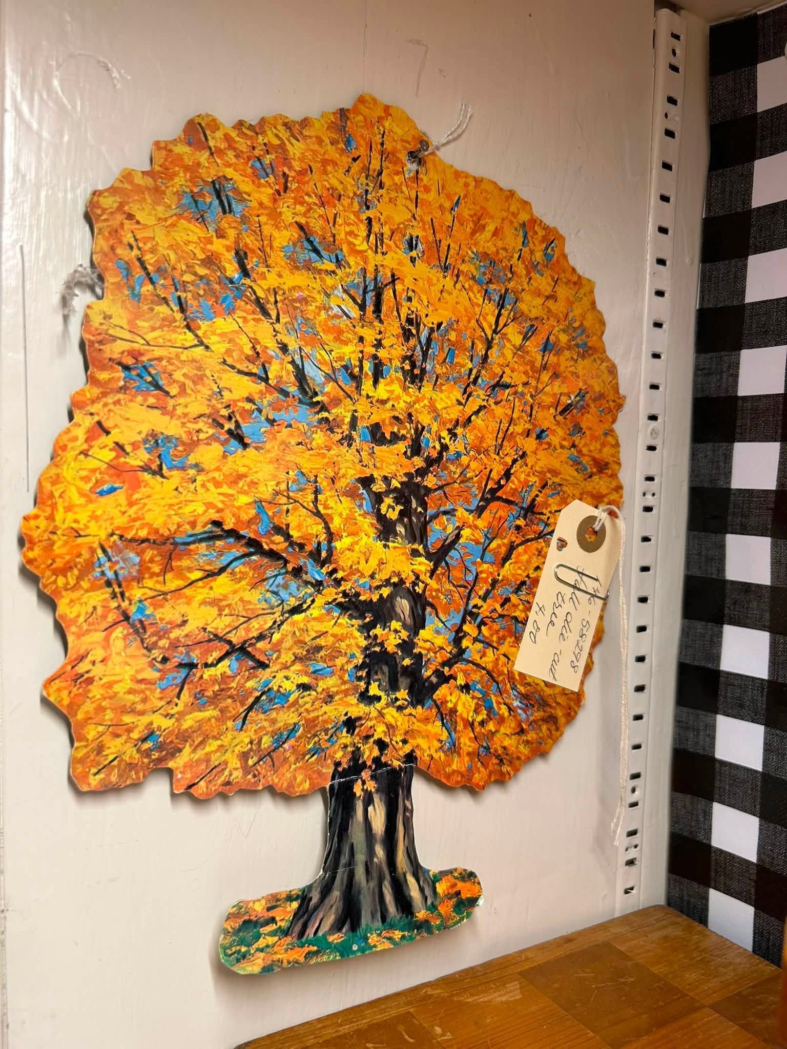 Orange and blue painted tree artwork on a wall, with a decorative hanging tag and a black trunk.