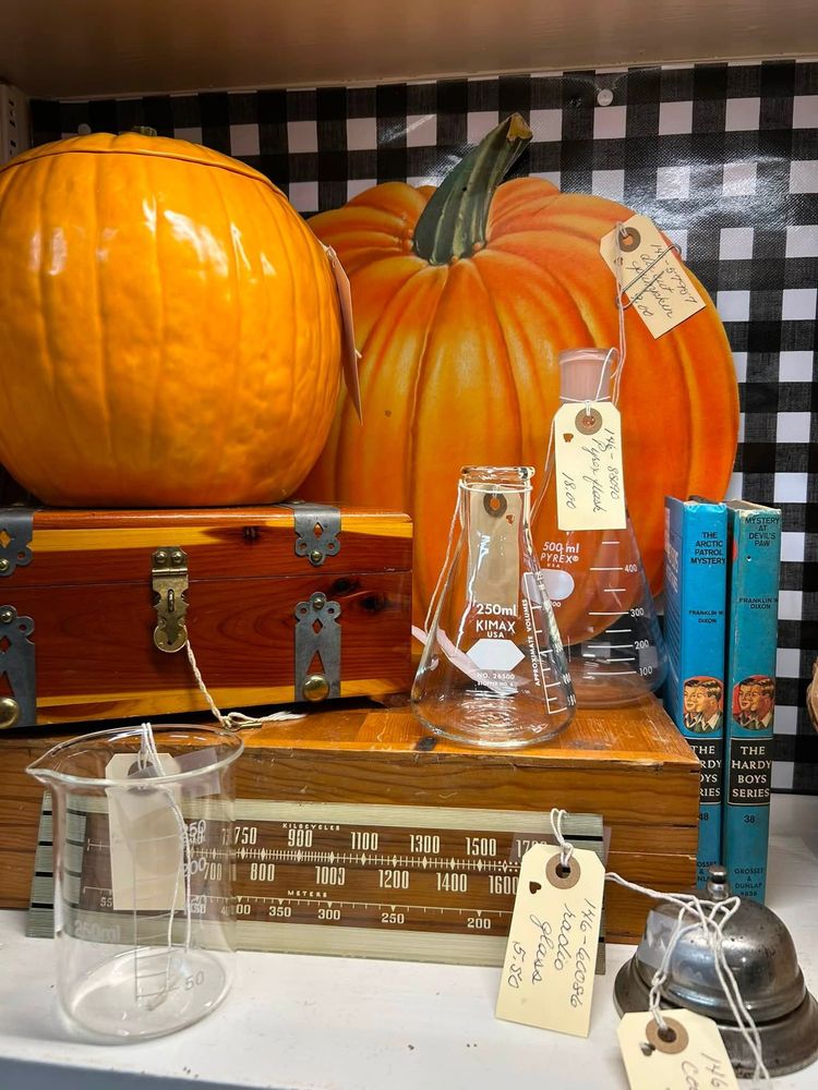 Pumpkins on stacked wooden trunks with glassware and antique items on a checkered cloth backdrop