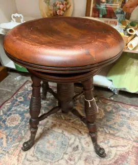 Antique wooden round stool with a worn brown seat and turned legs on a patterned rug