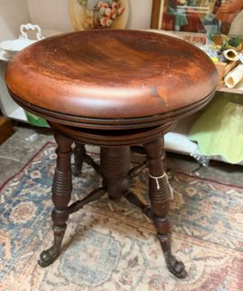 Antique wooden round stool with a worn brown seat and turned legs on a patterned rug