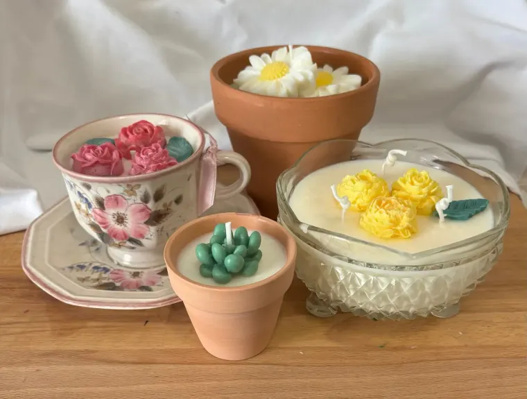 Small decorative candles in teacups and terracotta pots arranged on a wooden surface.
