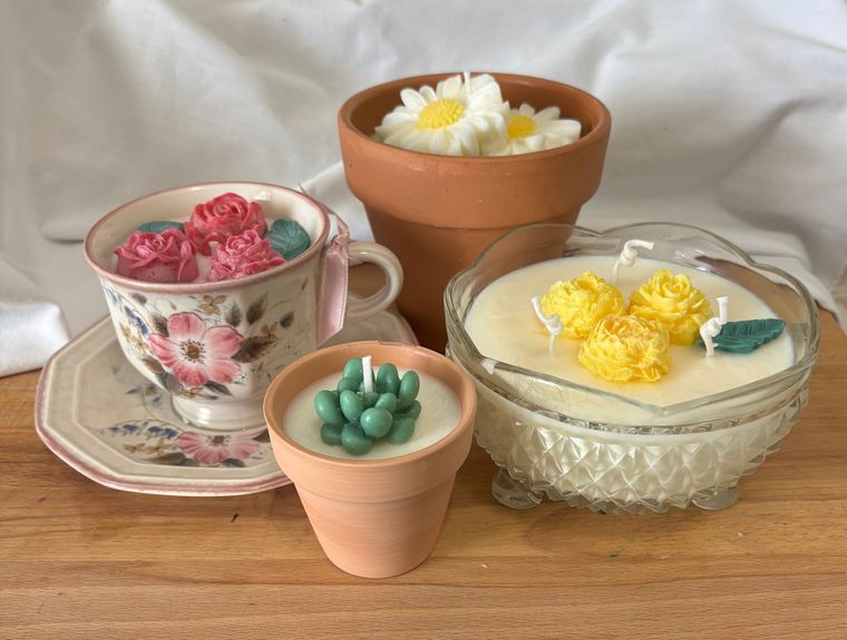 Small decorative candles in teacups and terracotta pots arranged on a wooden surface.