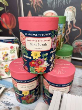 Floral tin candles with pink lids stacked on a table, including one labeled “Mini Petals”