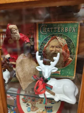 Holiday window display with a white reindeer figurine, burlap-wrapped Santa, and a green Catterbox tin box