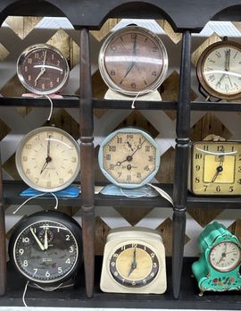 Assorted vintage clocks arranged in a wooden display shelf, each with a different face and style.