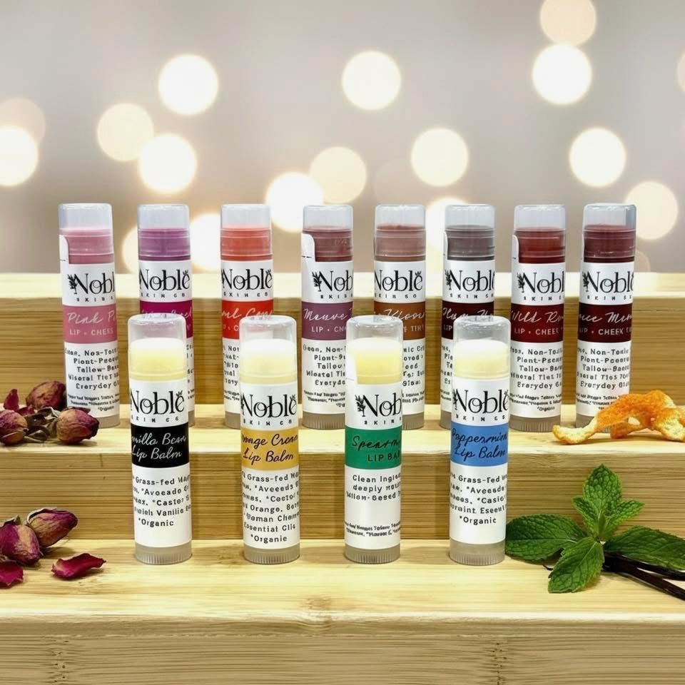 Assorted lip balm tubes displayed on a wooden tray with flowers and soft bokeh lights in the background