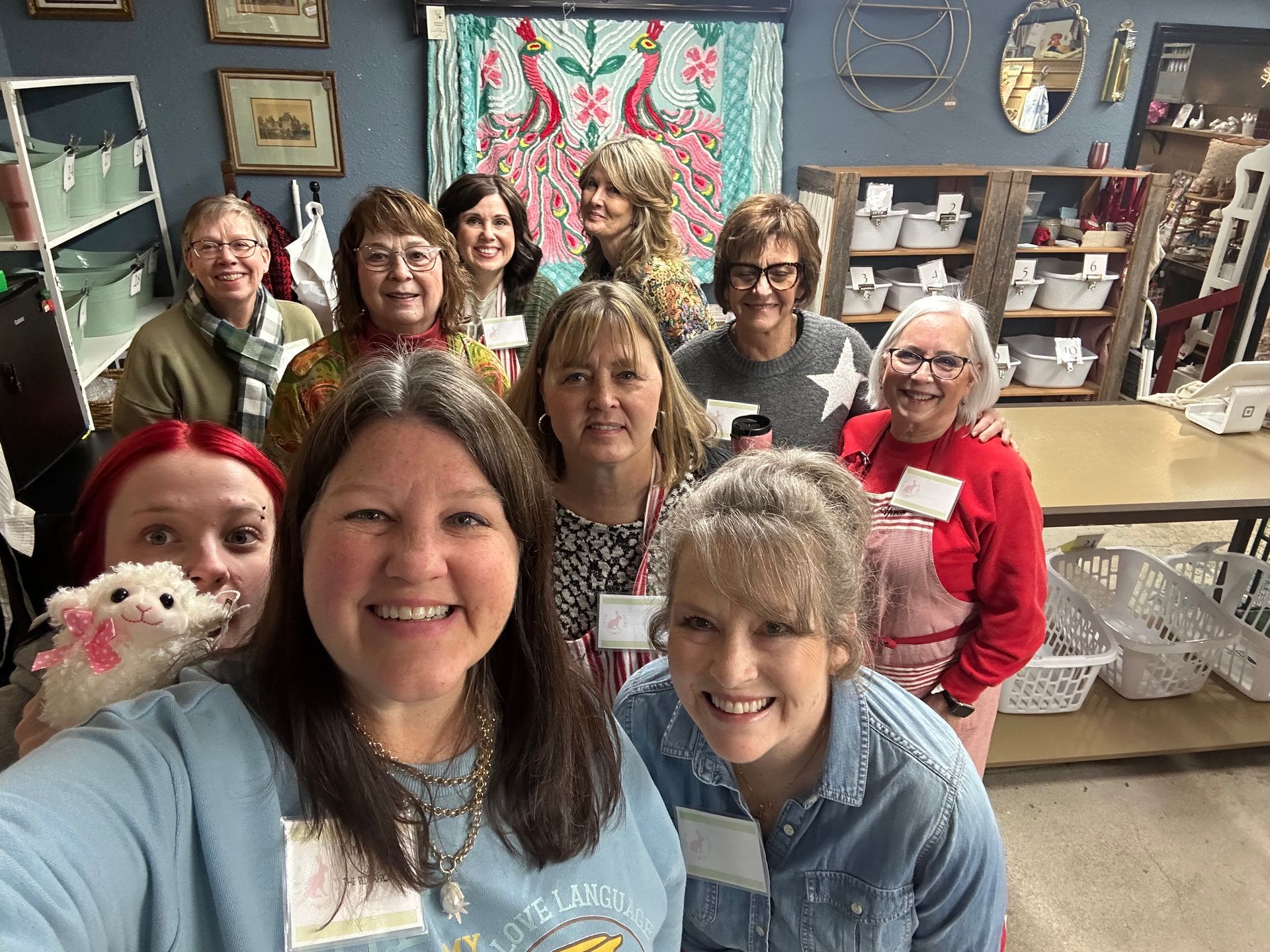 Group of smiling people posing in a cozy craft room, with quilts and decor in the background.