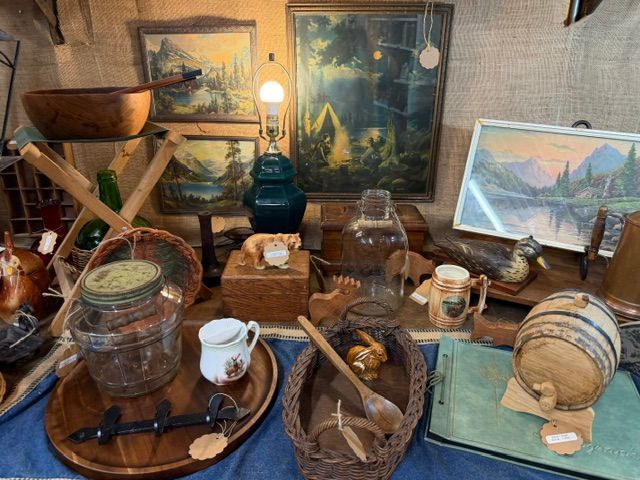 Vintage tabletop display with jars, bowls, a lantern, and framed landscape art in a rustic room
