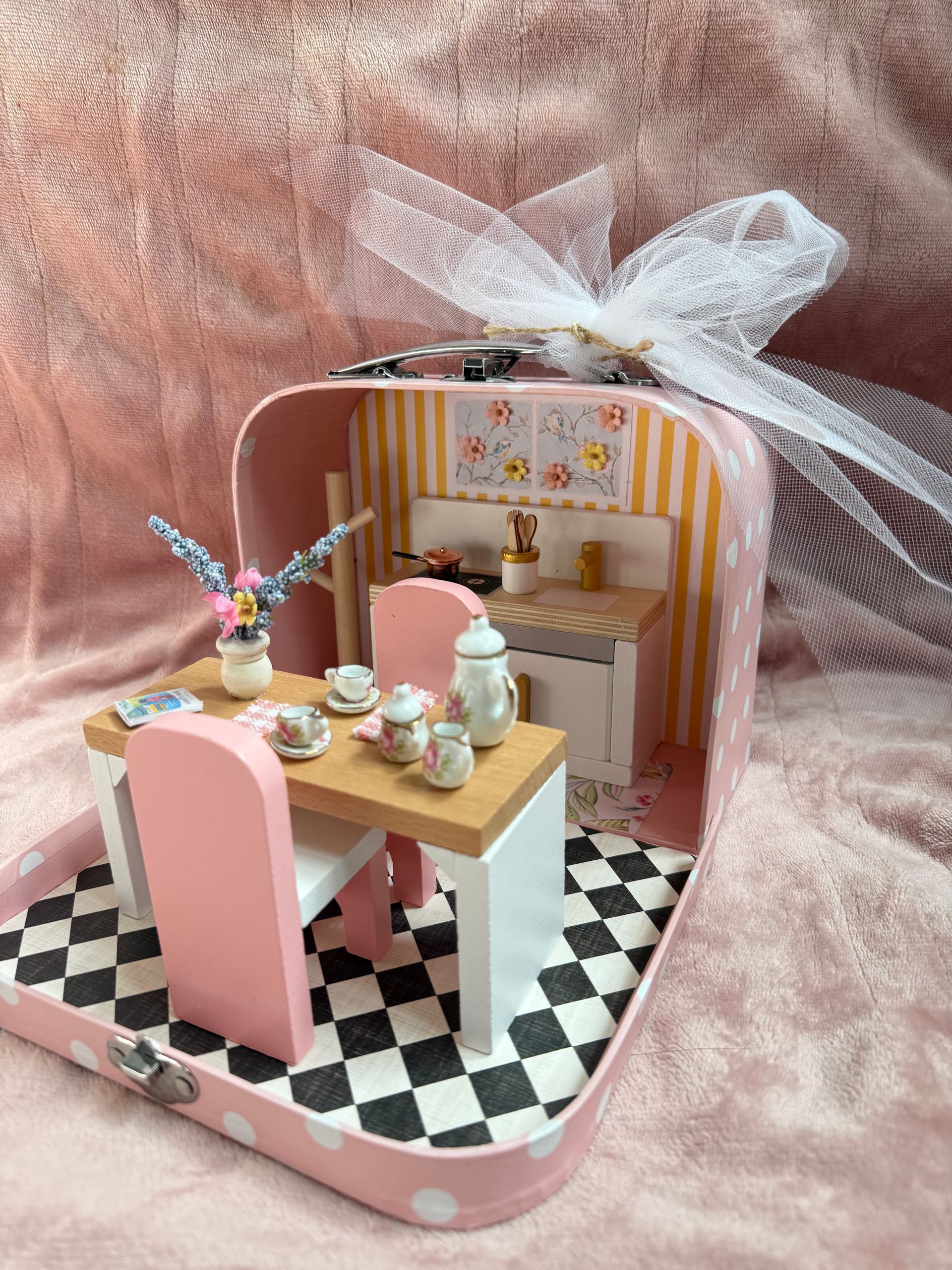 Miniature pink-and-white dollhouse room with tiny table, chairs, and decor on a pink background