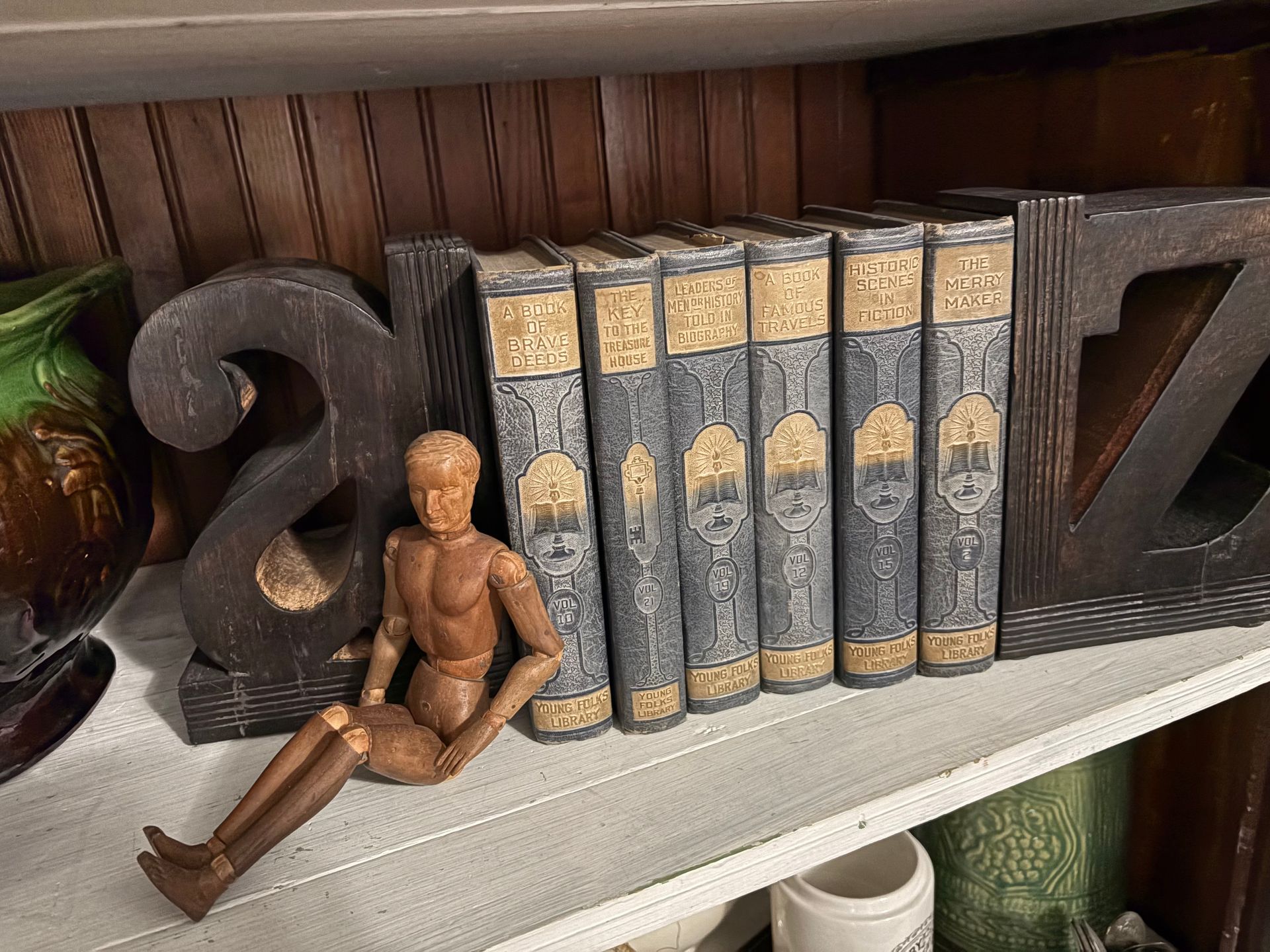 Wooden figurine leaning against decorative books on a shelf beside carved bookends
