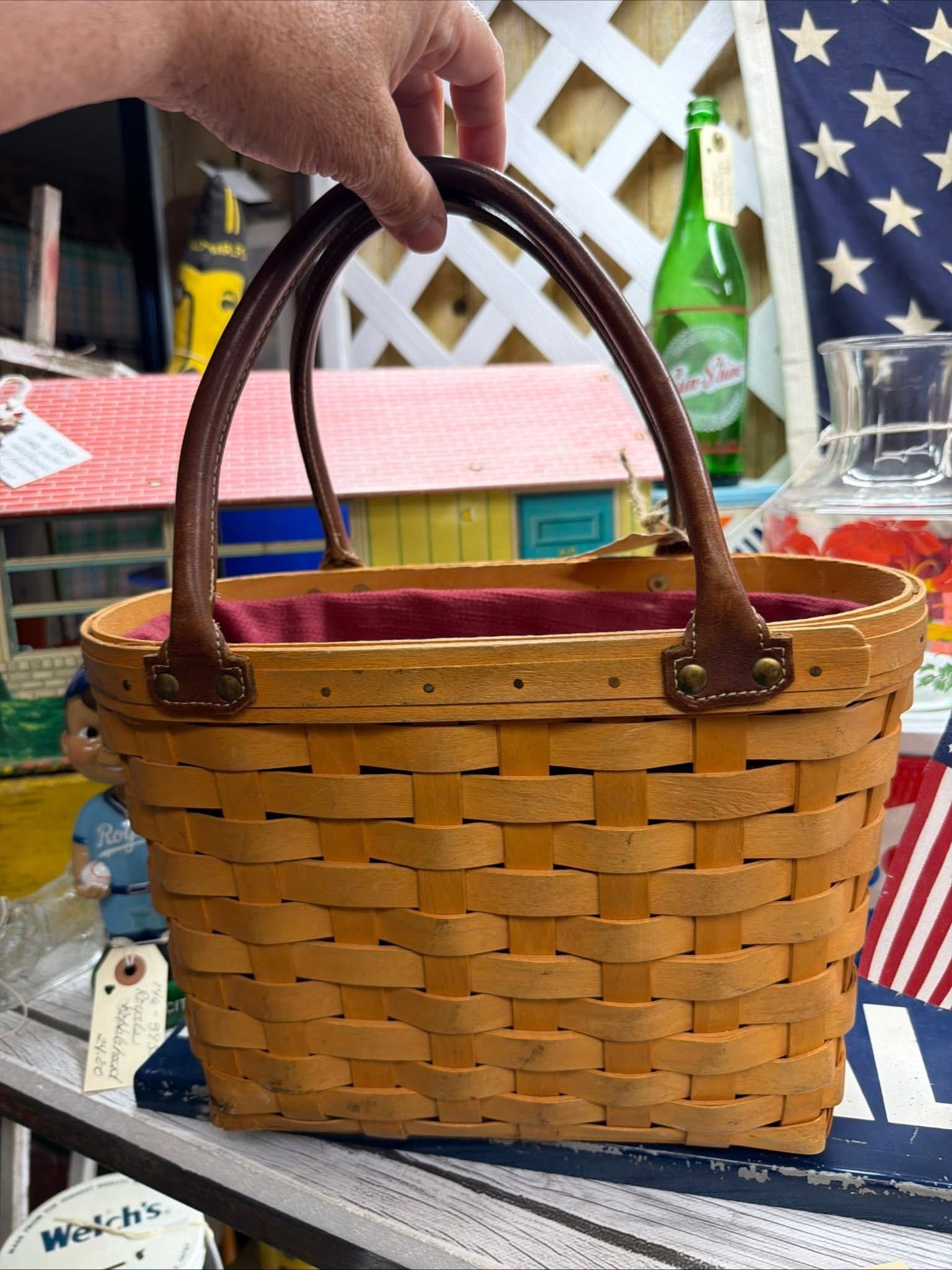 Hand holding a small woven basket with brown handles on a table outdoors