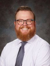 A man with a beard and glasses is wearing a hat and smiling.
