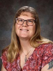 A woman wearing glasses and a blue jacket is smiling for a picture.