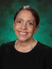 A woman in a black shirt is smiling in front of a green background.