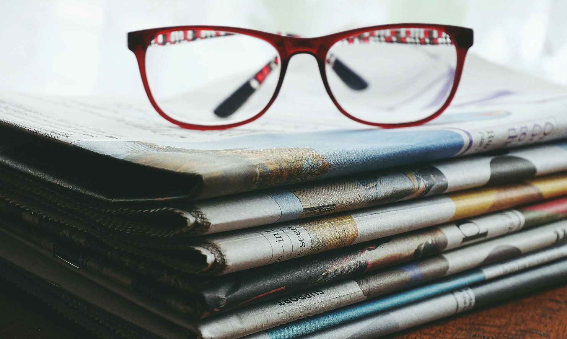 A pair of glasses is sitting on top of a stack of newspapers.