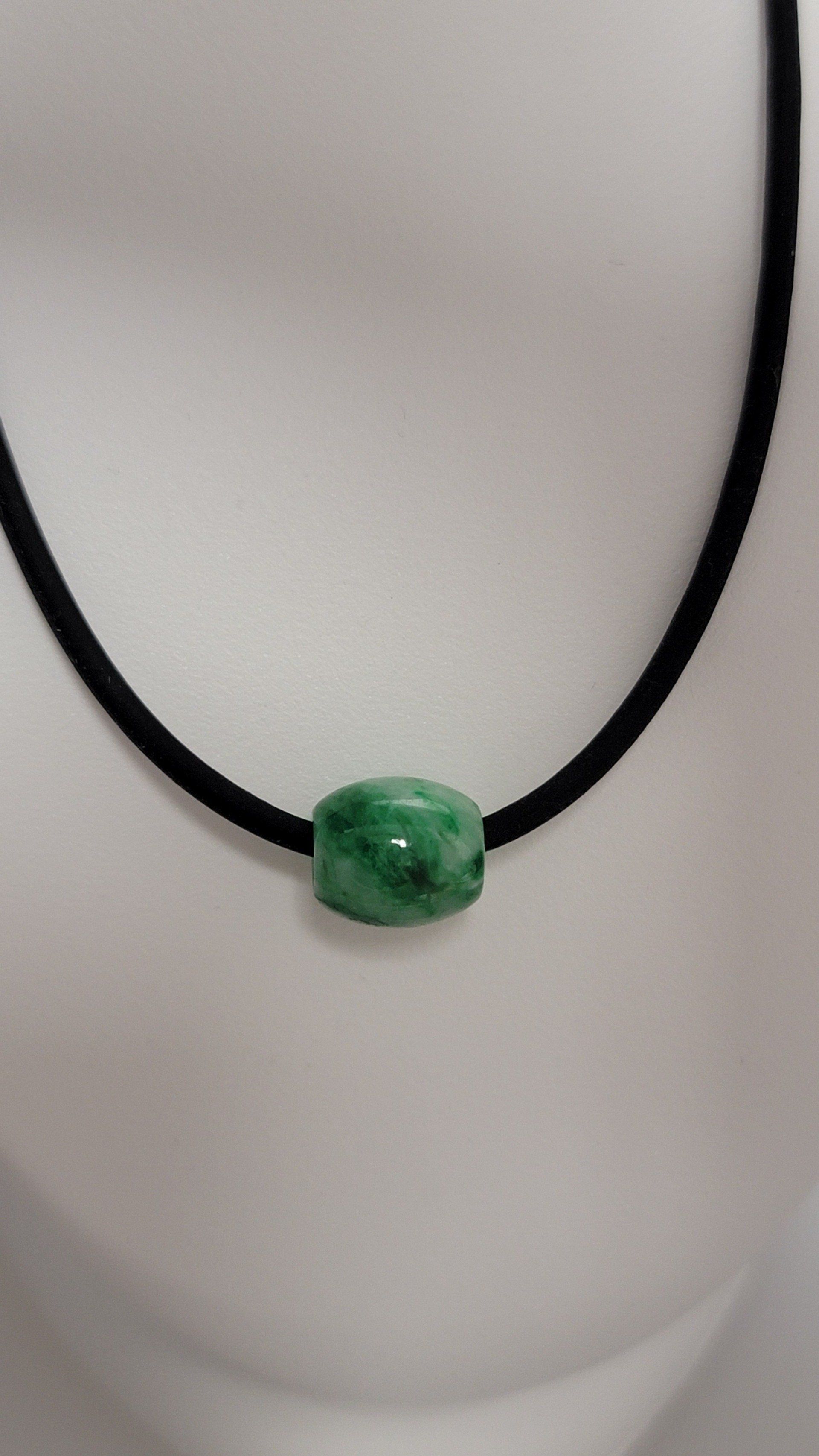Green jade bead pendant on a black cord necklace against a white background.