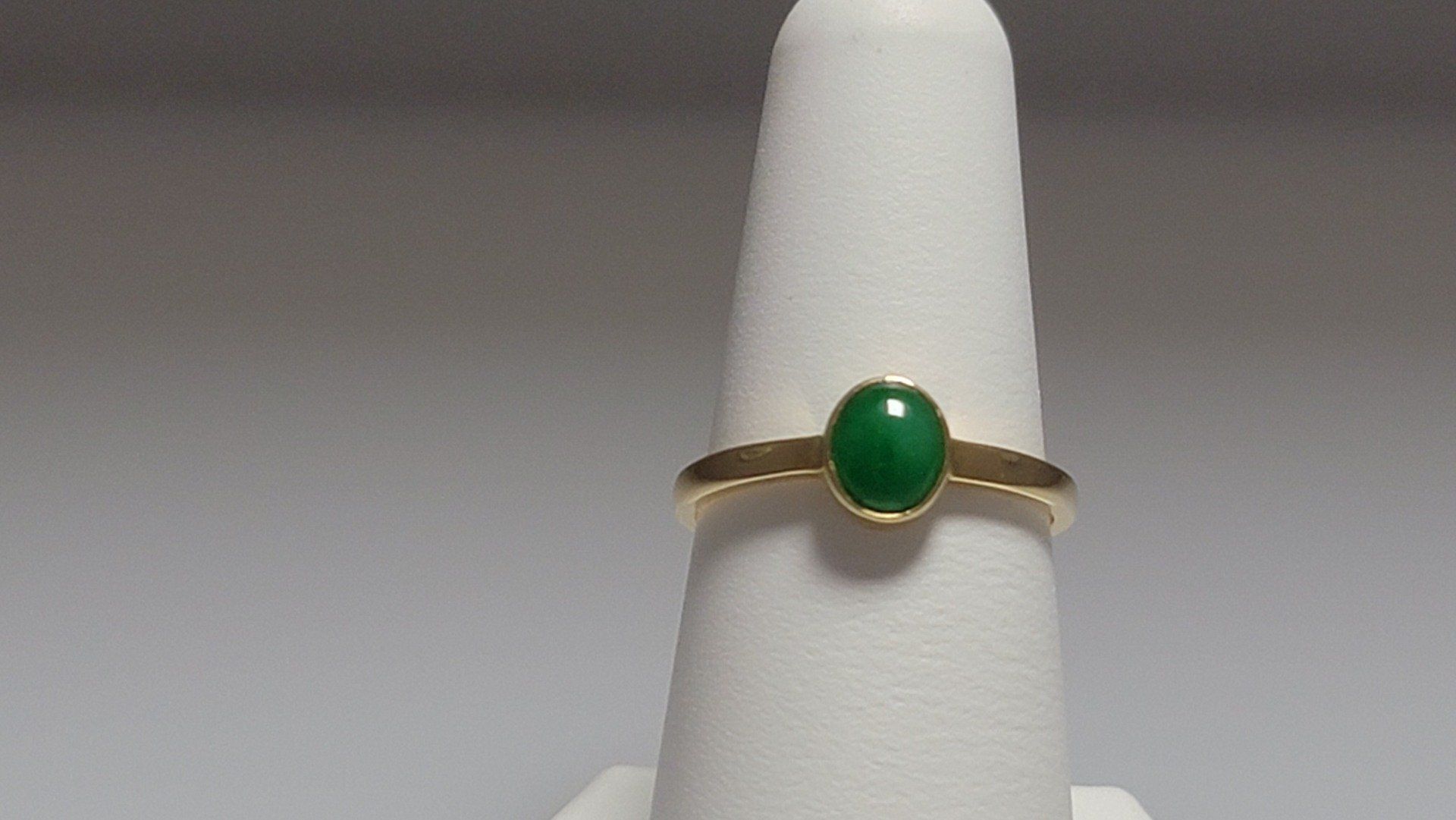 Gold ring with an oval, green gemstone on a white finger-shaped display.