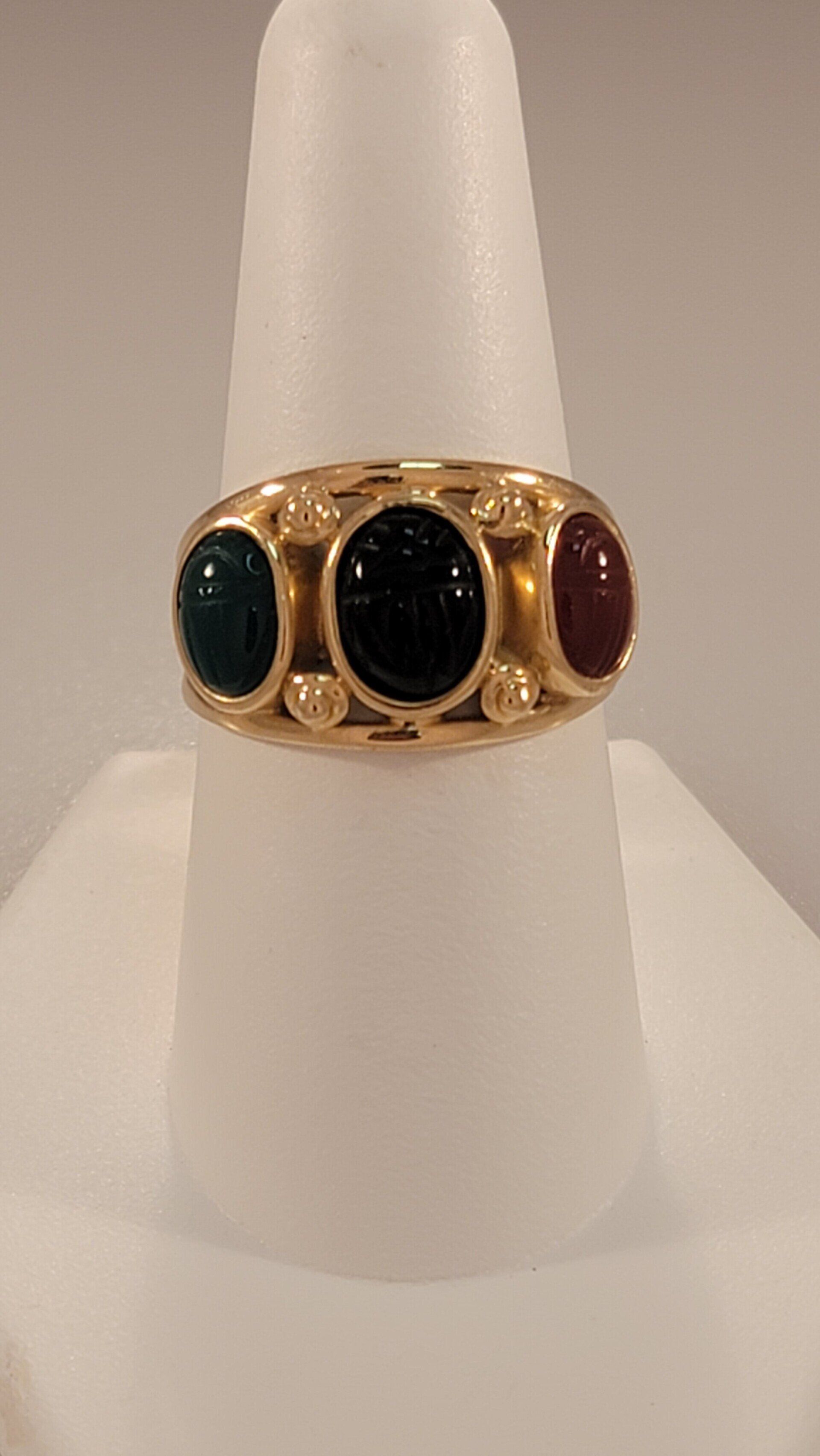 Gold ring with three oval gemstones: green, black, and red.