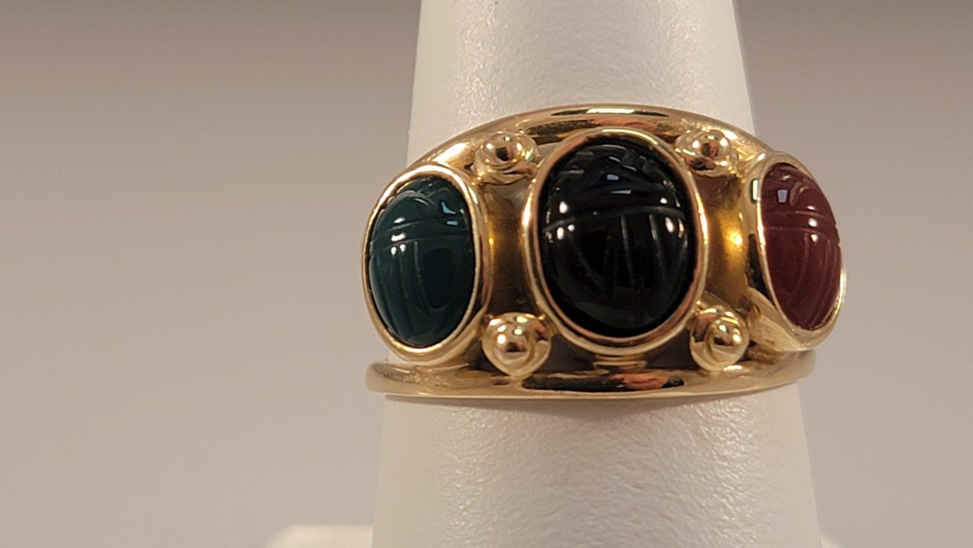 Gold ring with three oval-shaped scarab beetles in green, black, and red.