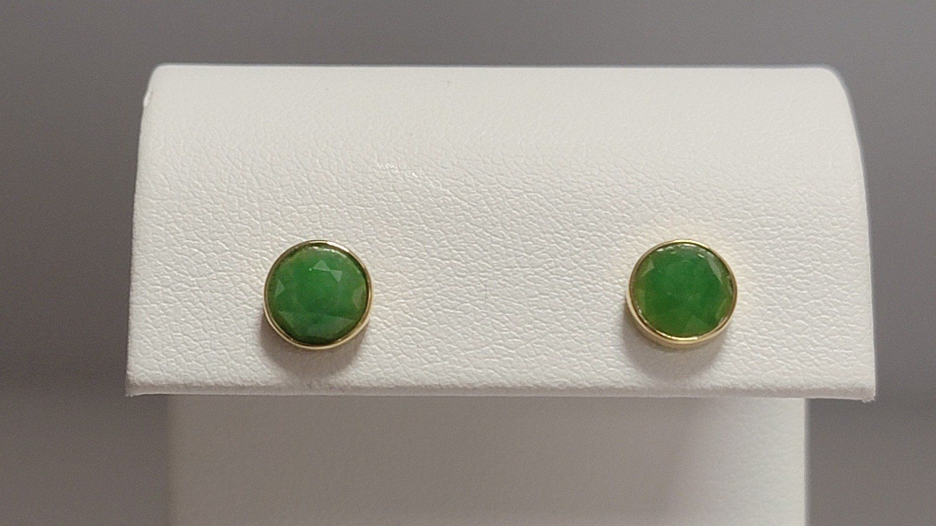 Gold stud earrings with round, green gemstones on a white display stand.