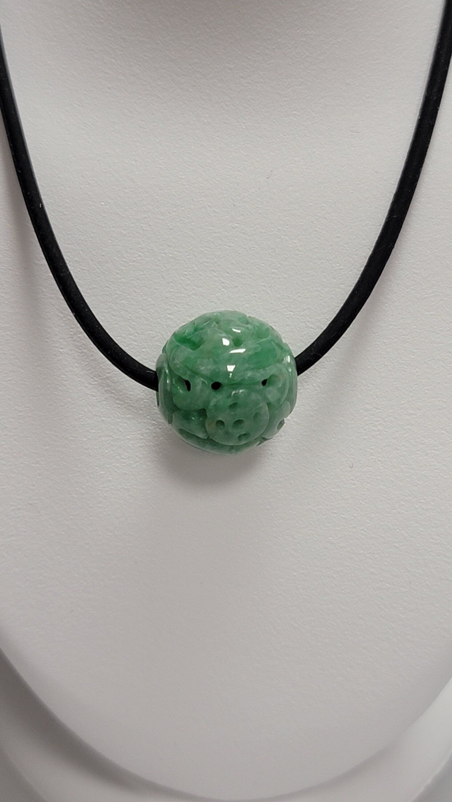Green carved jade pendant necklace on a black cord.