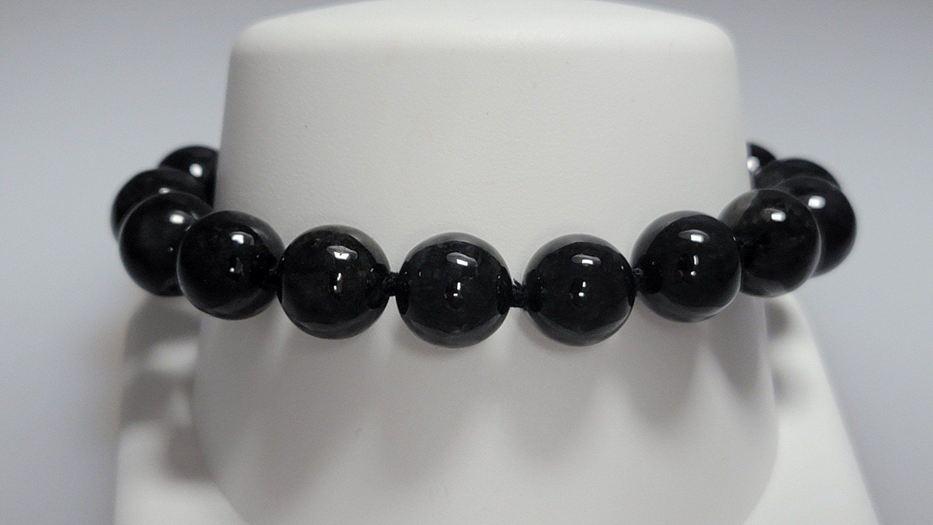 Black beaded bracelet on a white display stand.