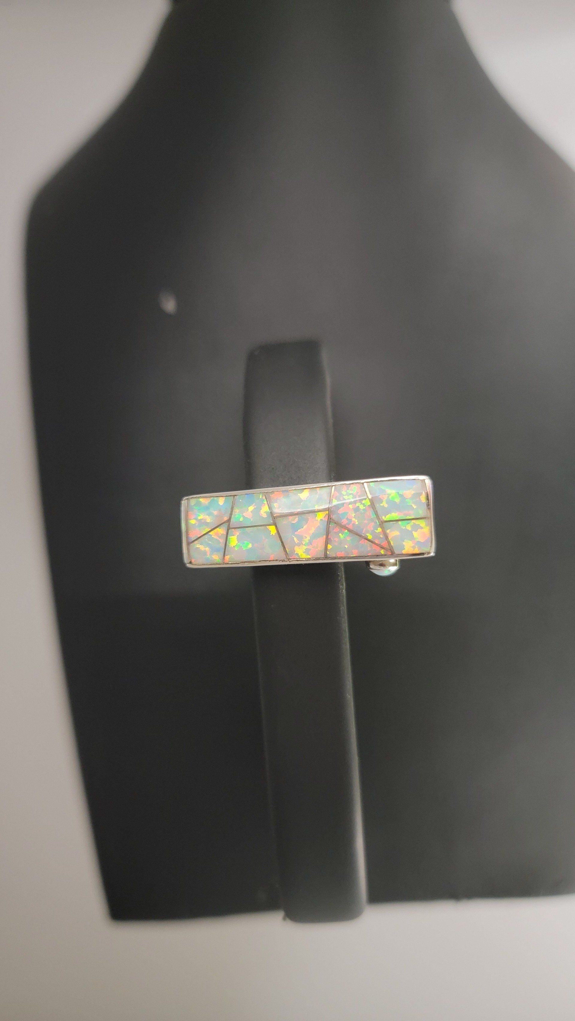 A rectangular opal ring on a black jewelry stand, displaying a mosaic pattern and iridescent colors.