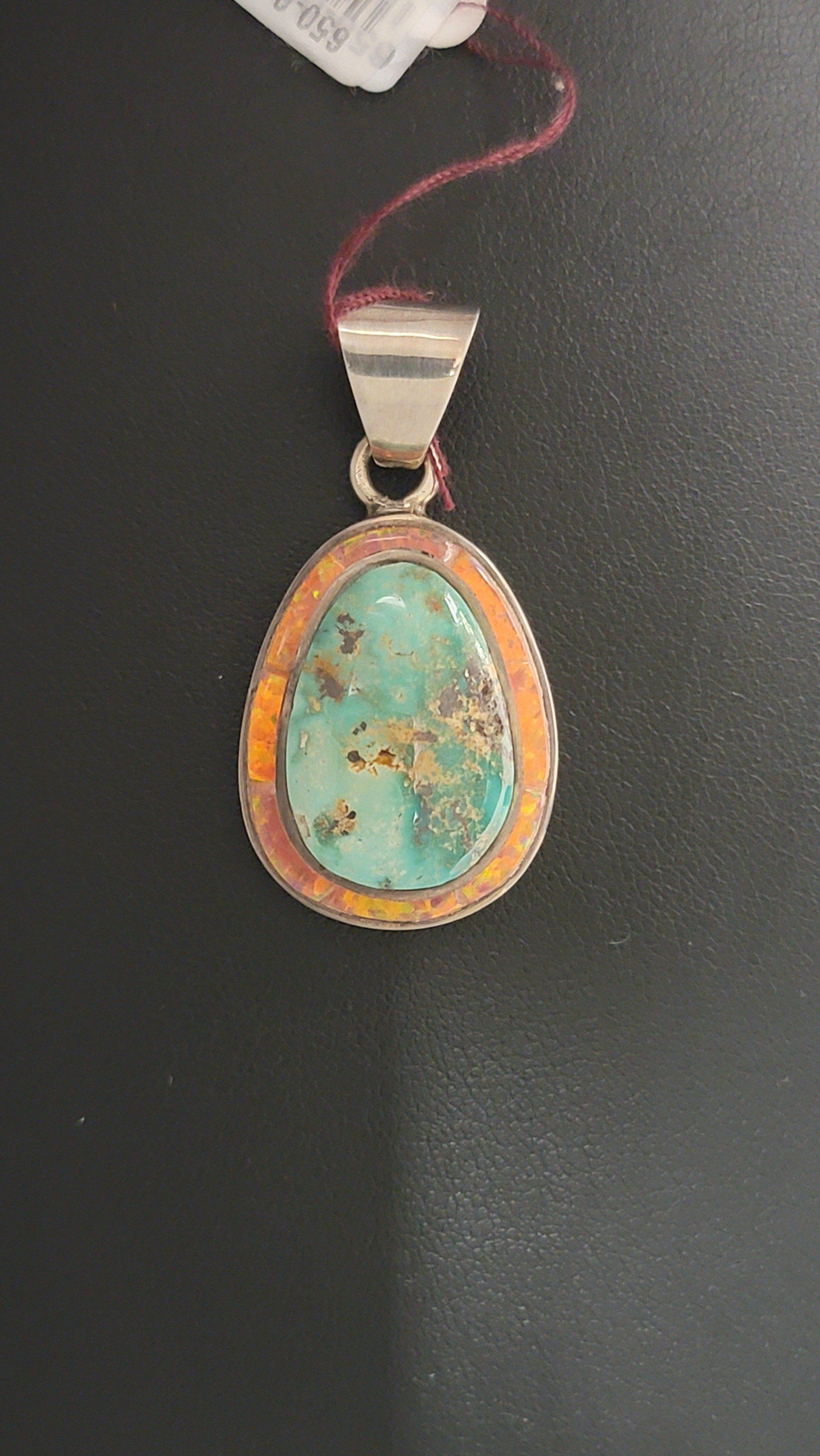 Teardrop-shaped turquoise pendant with orange and silver accents, on a dark background.