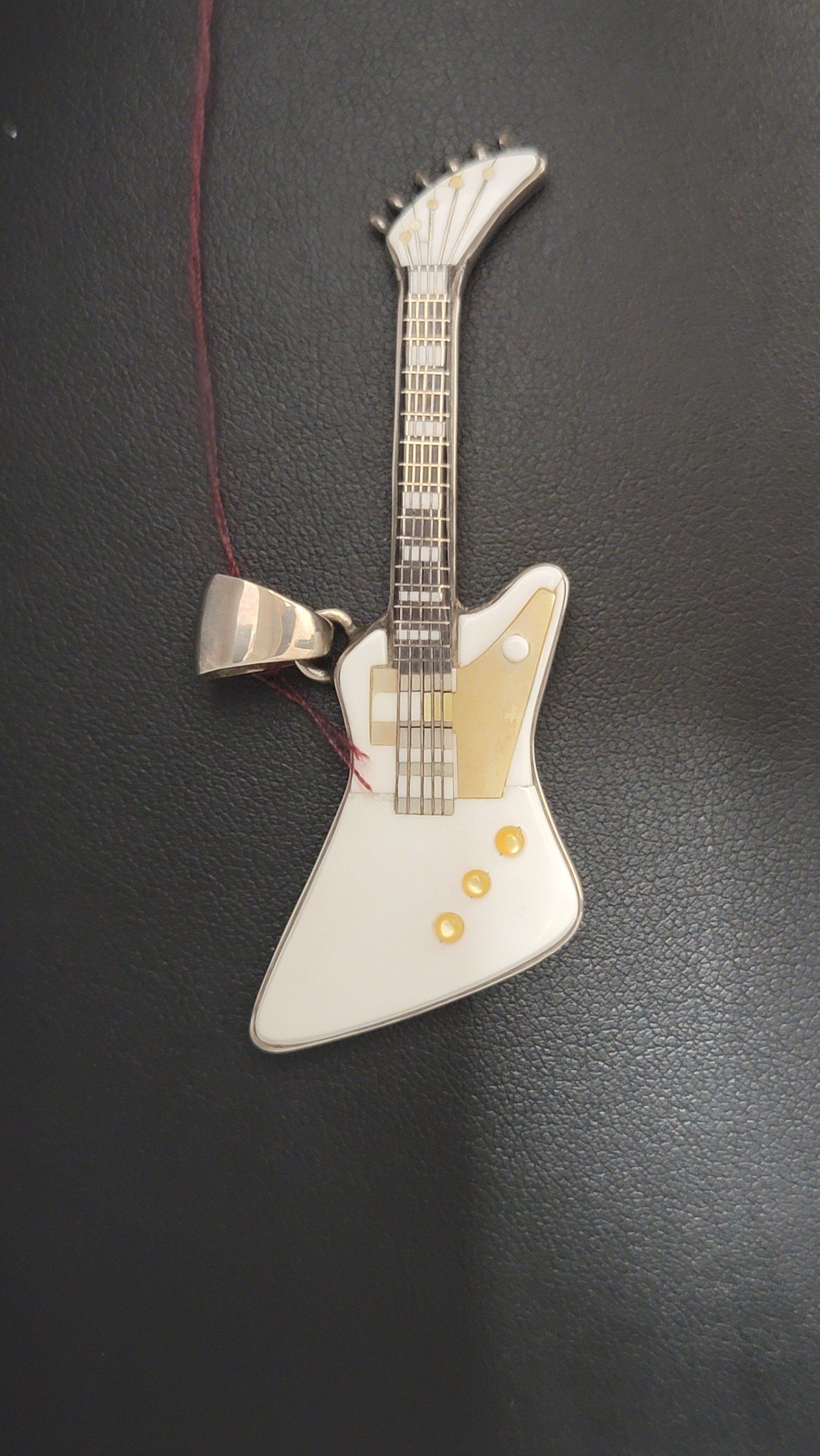 White and gold guitar pendant hanging on a dark surface.