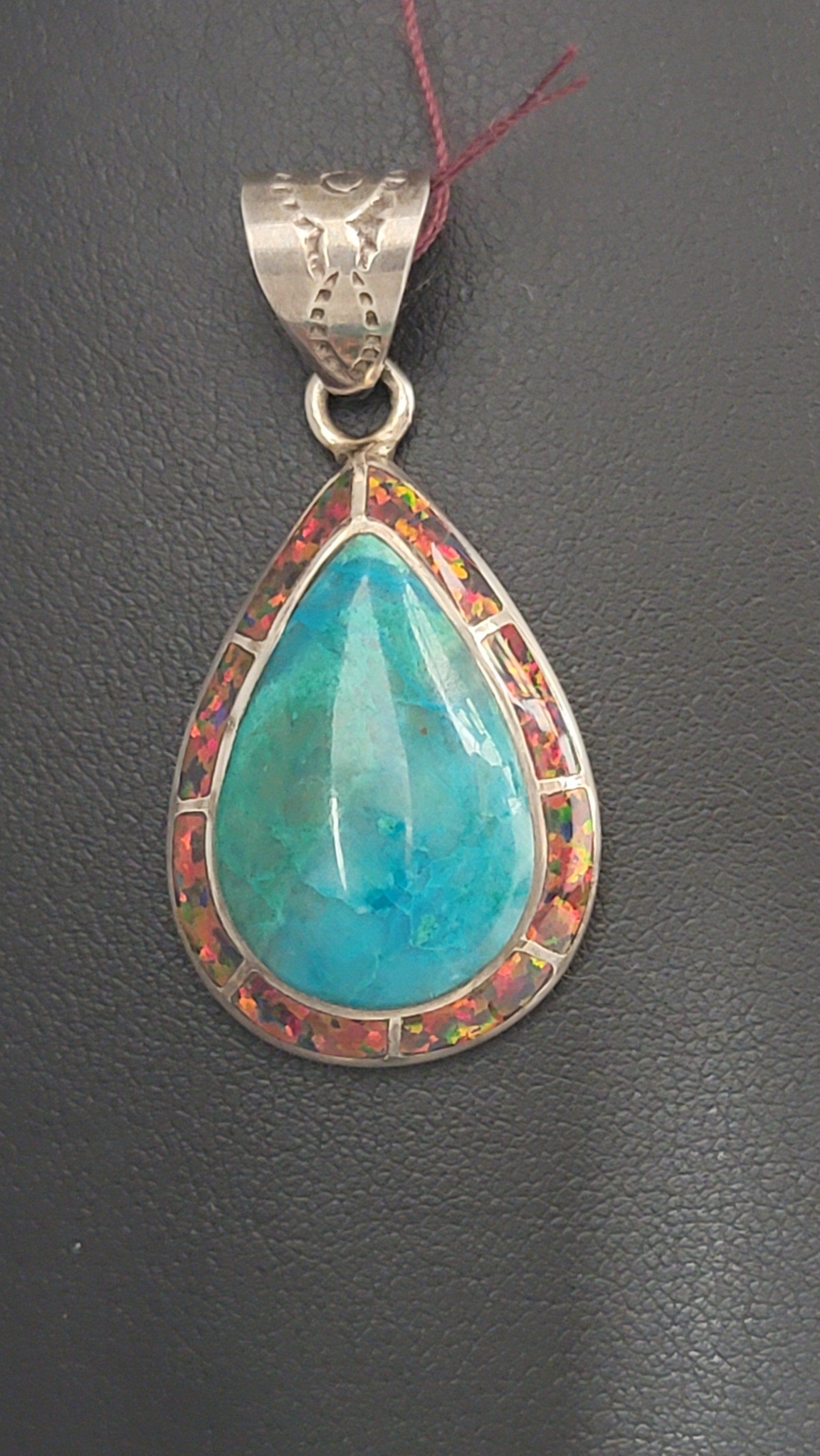 Teardrop pendant with blue-green stone, red border, and silver bail on a black background.