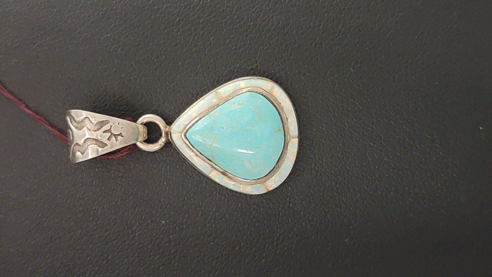 Teardrop-shaped turquoise pendant with silver detailing, on a black background.