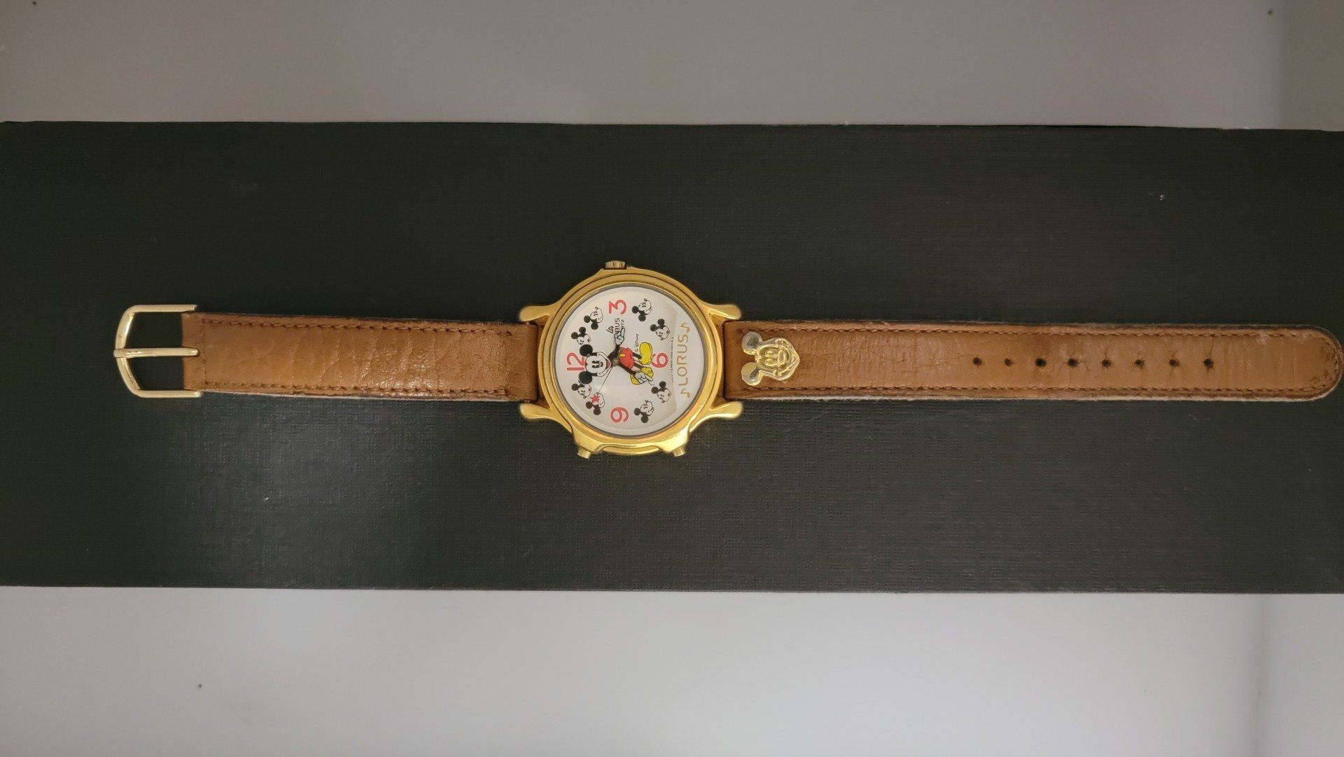 Mickey Mouse watch on a brown leather band, gold bezel, black and white face.