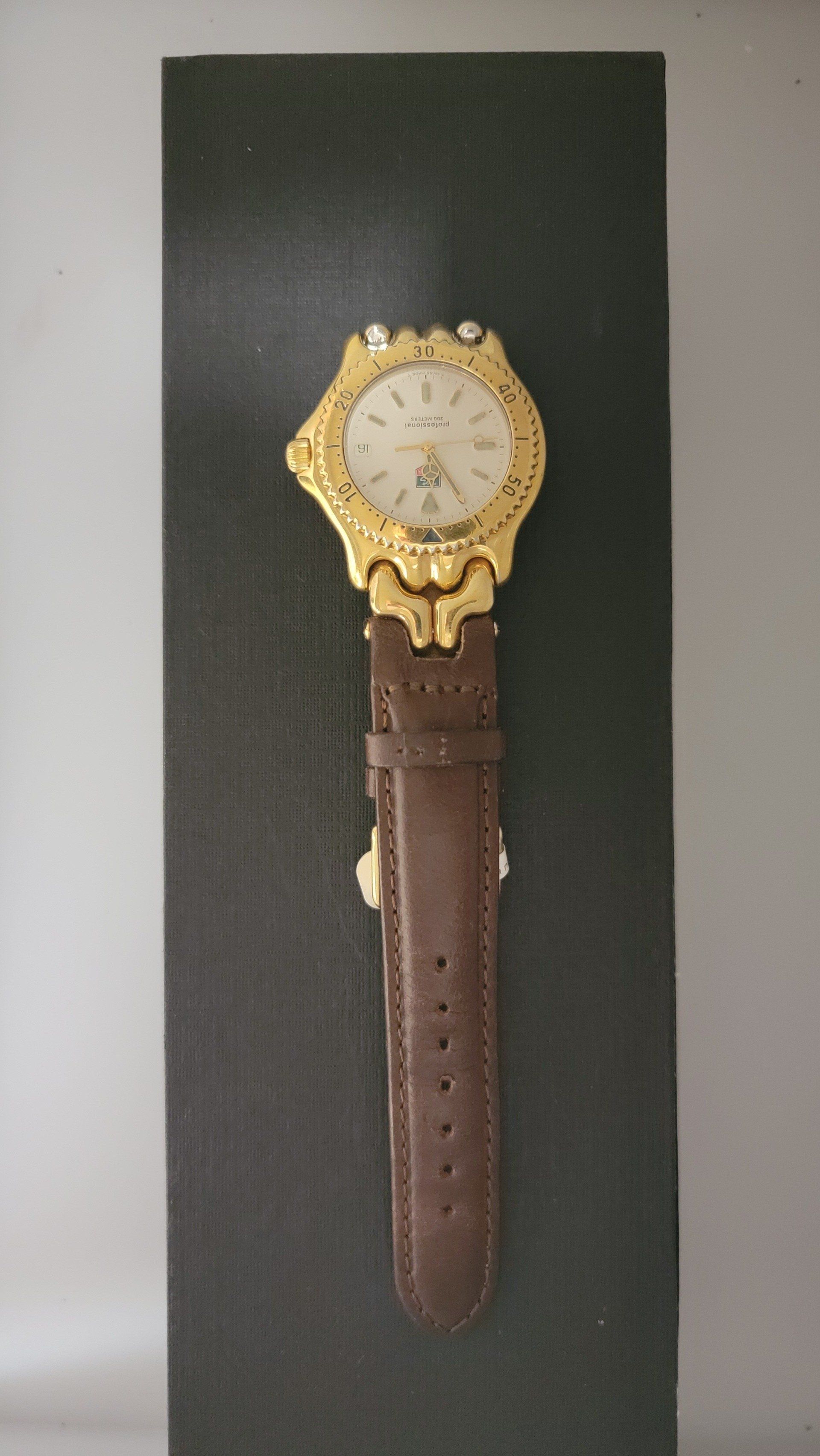 Gold wristwatch with brown leather strap on a black box.