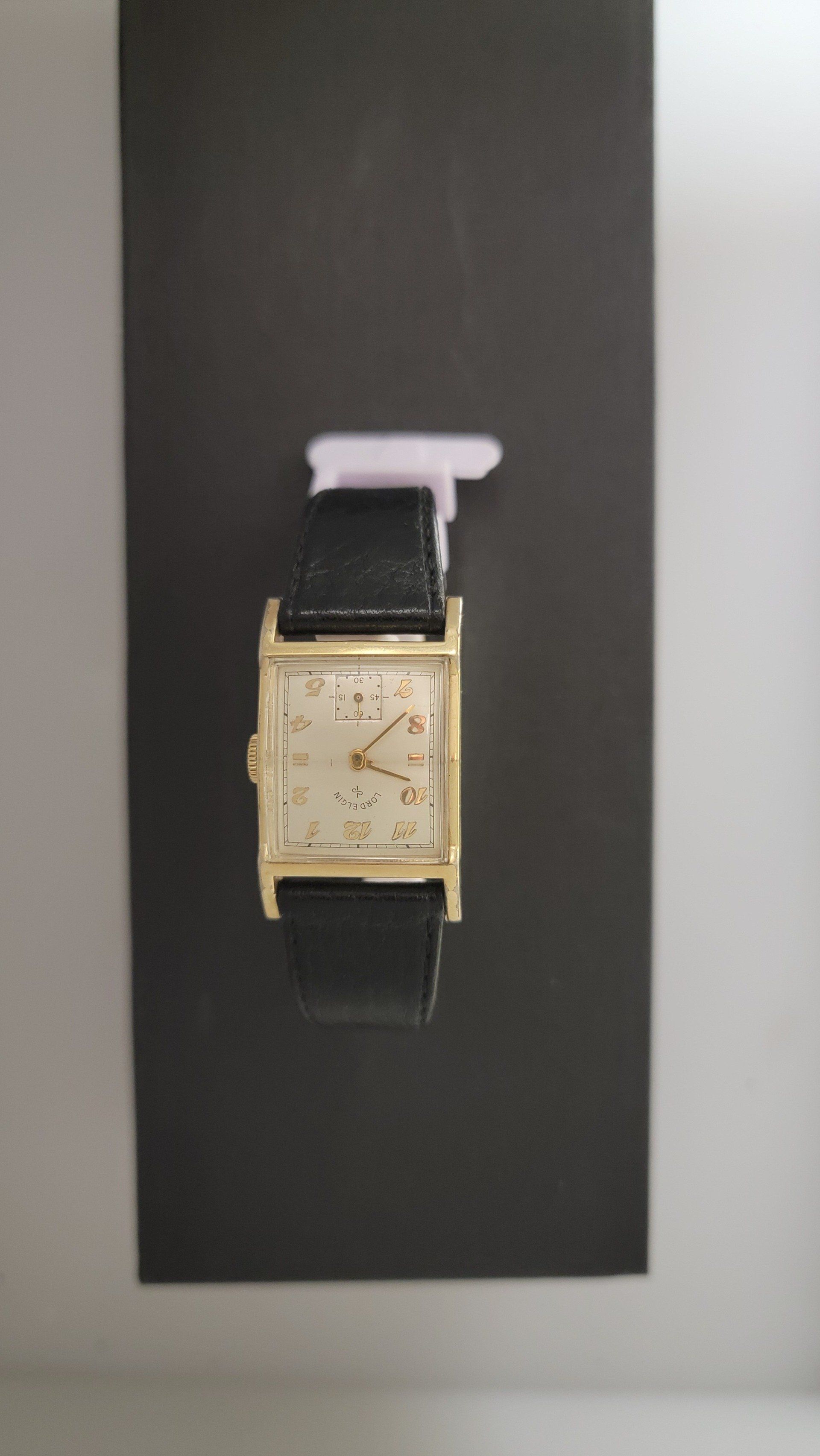 Gold rectangular wristwatch with black leather strap on a black display.