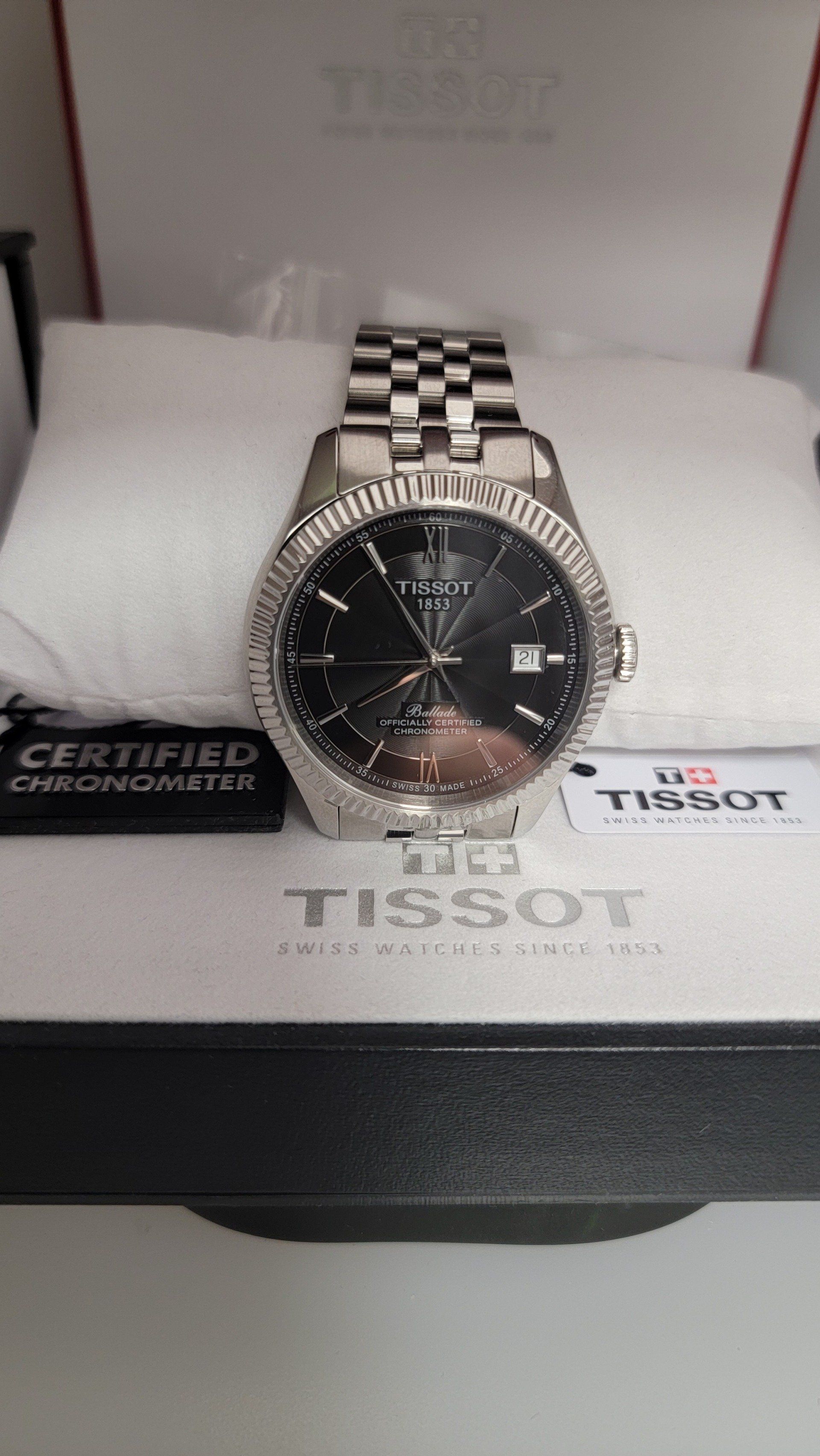Silver Tissot watch with a black face and stainless steel bracelet in its box.