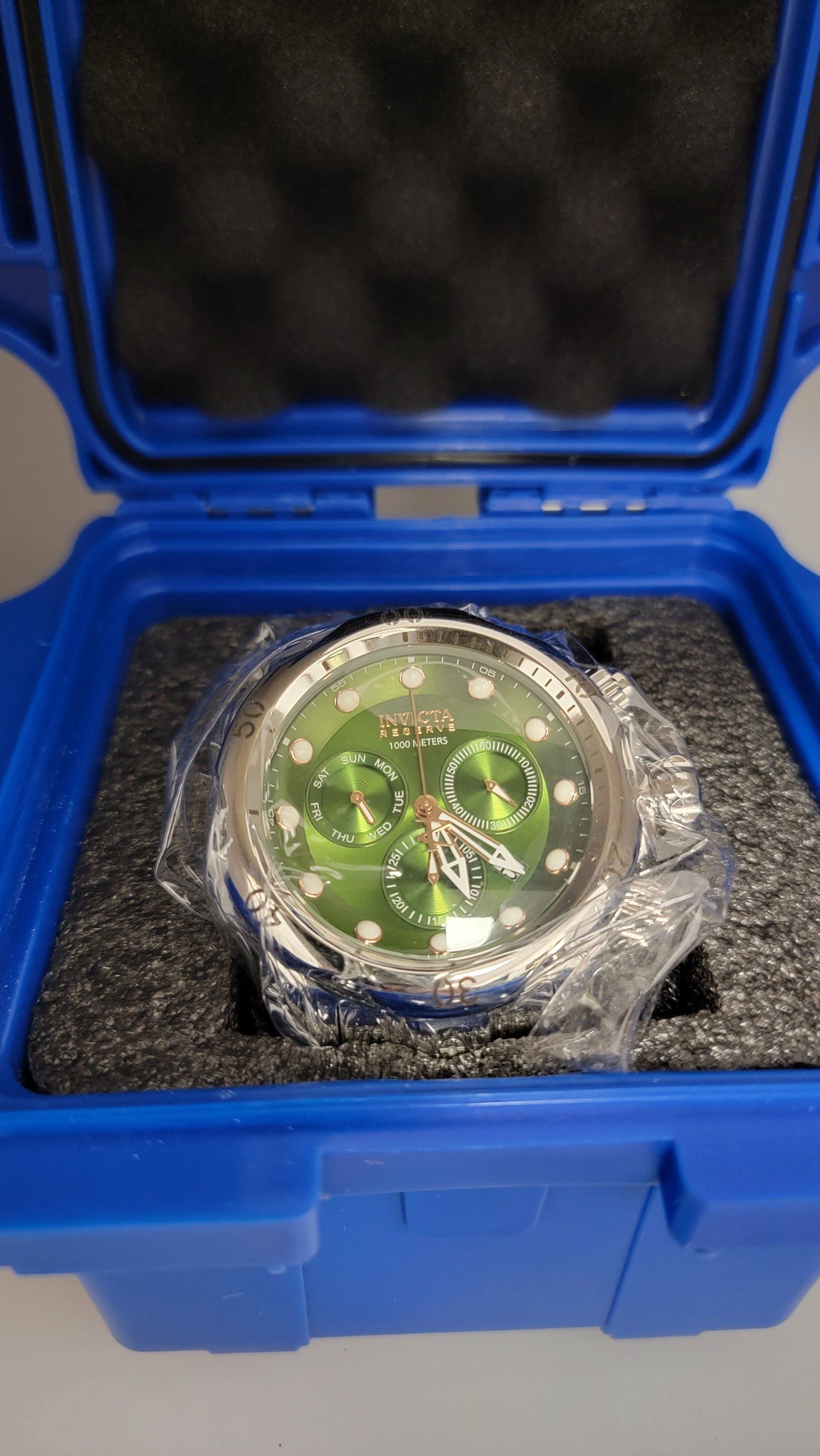 Green-faced wristwatch, protected in blue case with foam padding.