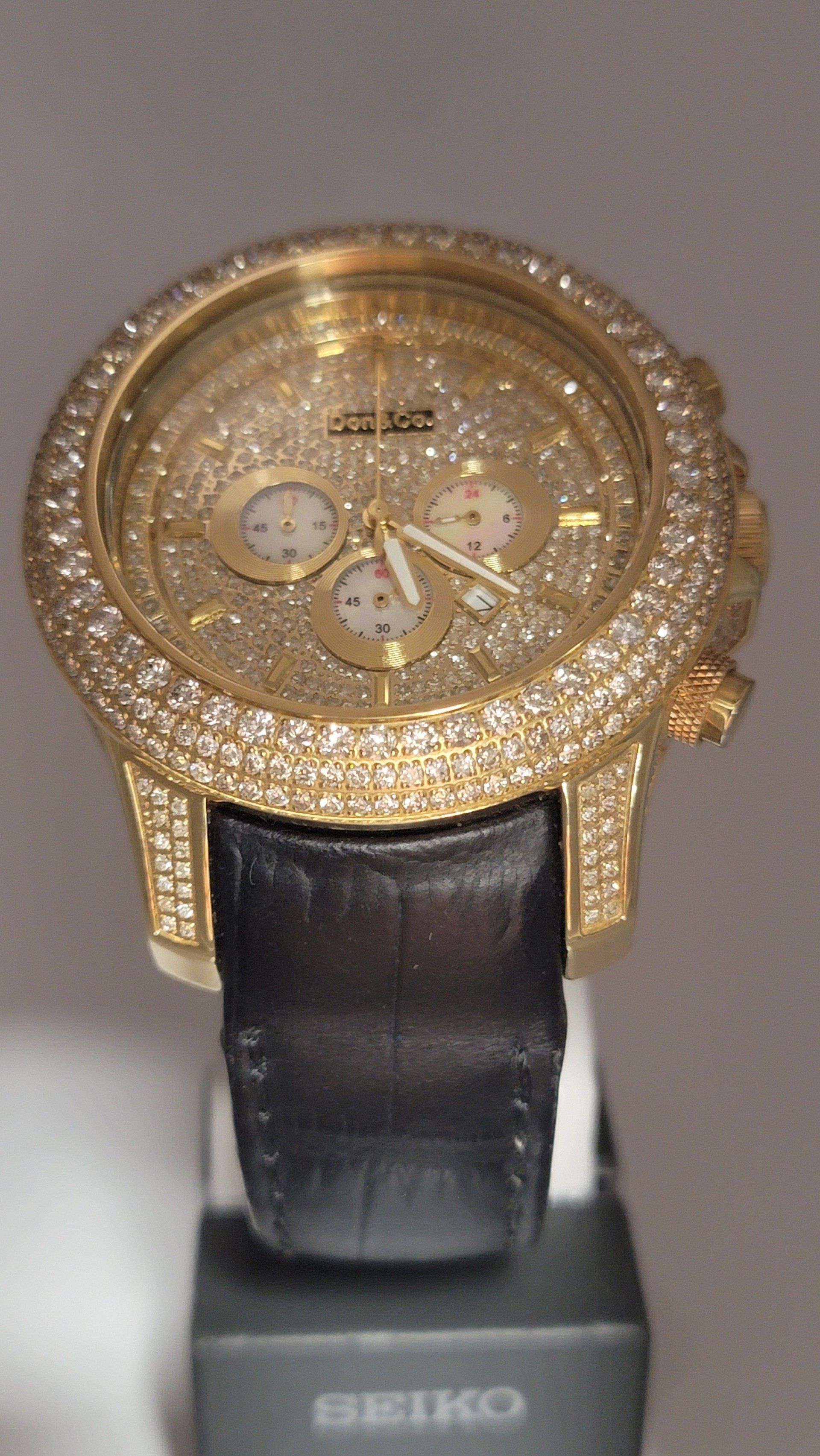 Gold watch with a diamond-studded face, bezel, and band details. Black leather band.