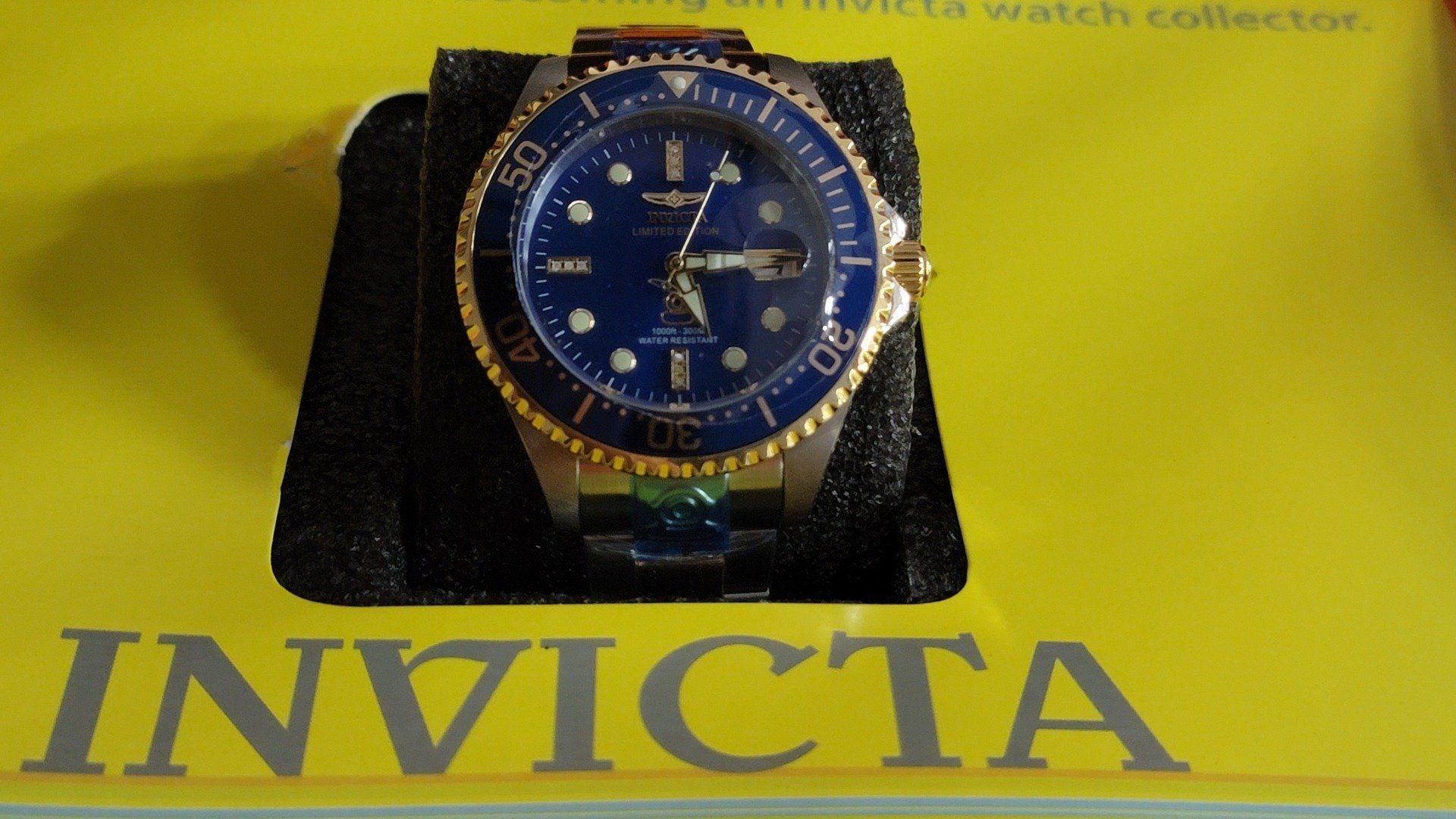 Invicta watch with a blue dial and gold bezel on a yellow box.
