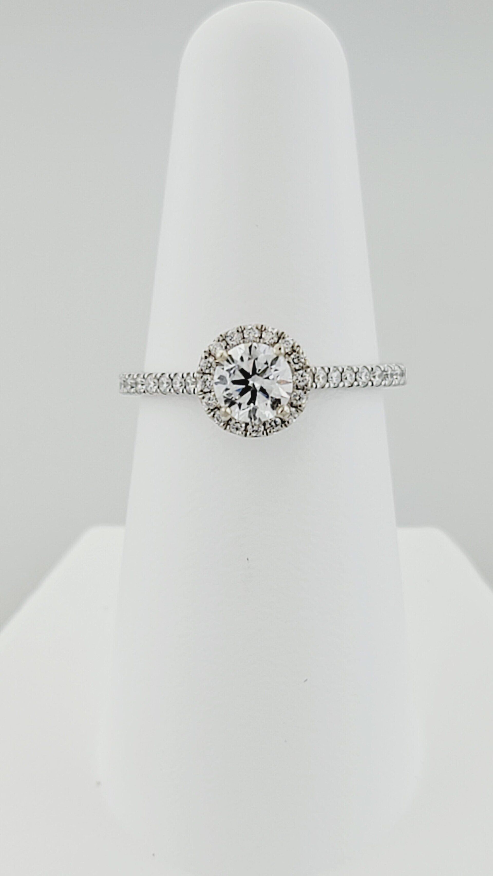 Diamond halo engagement ring on a white display stand.