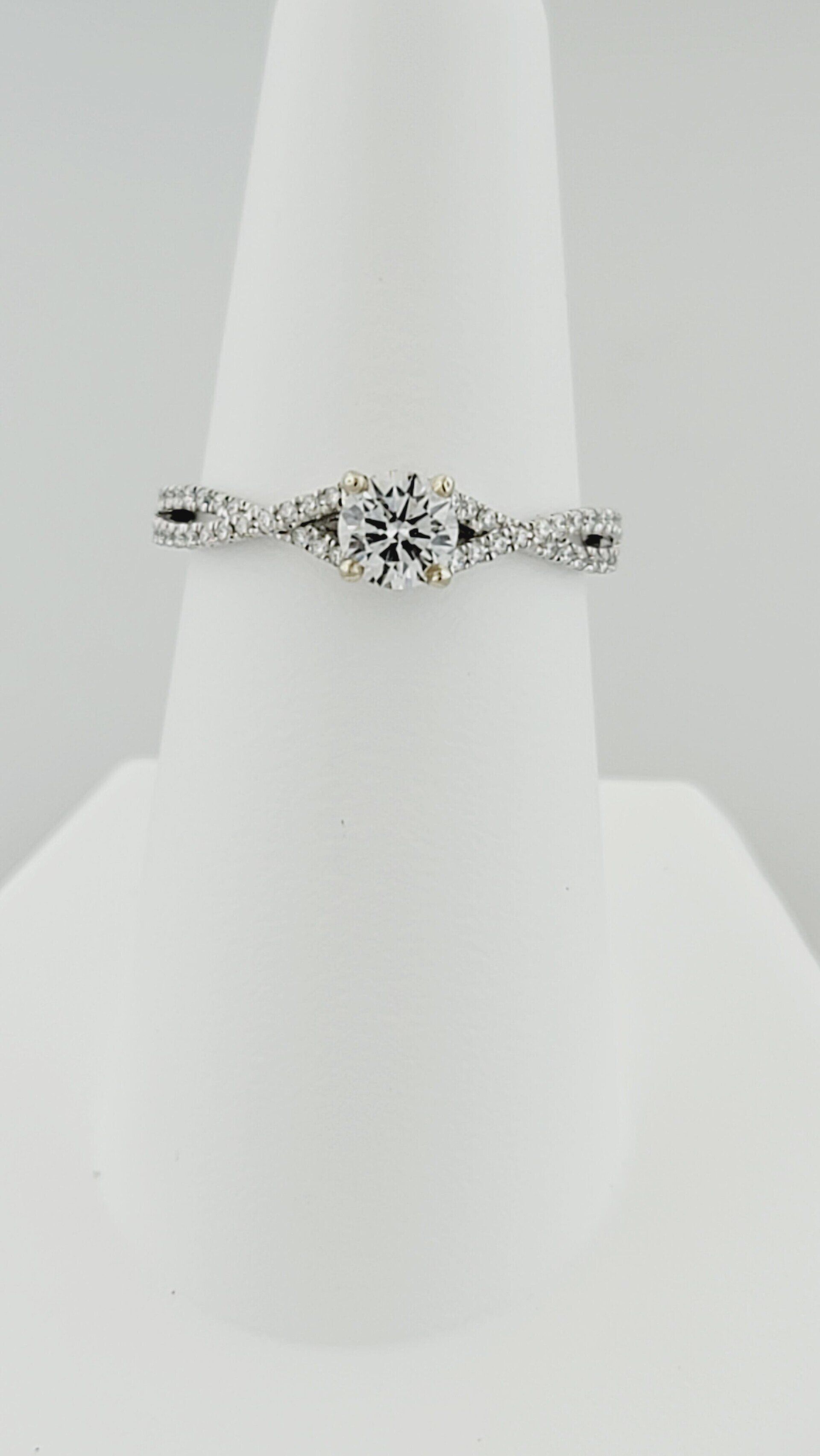 Diamond engagement ring on white display stand.