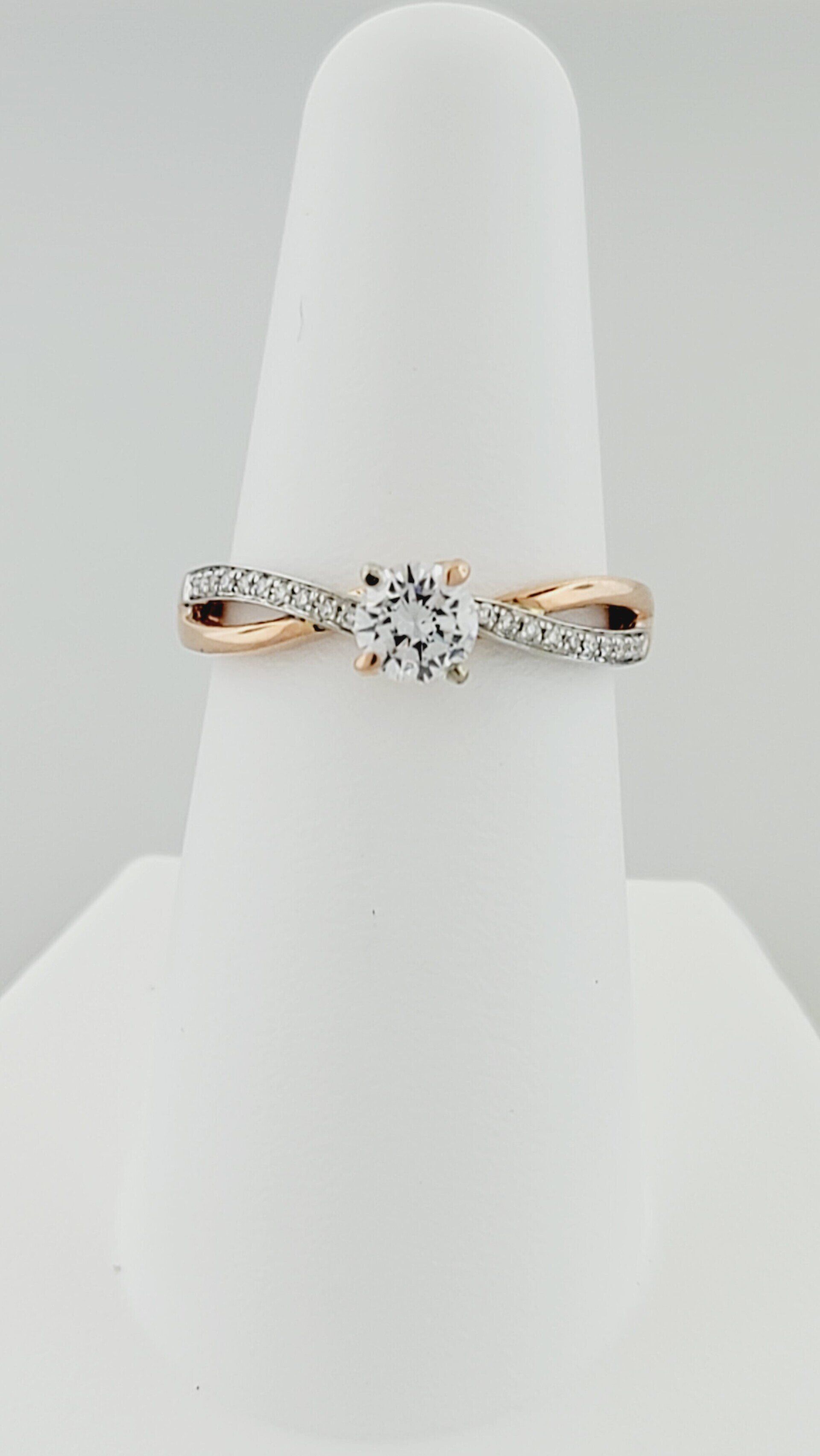 Rose gold engagement ring with a large, clear center stone and diamond accents on a white display stand.