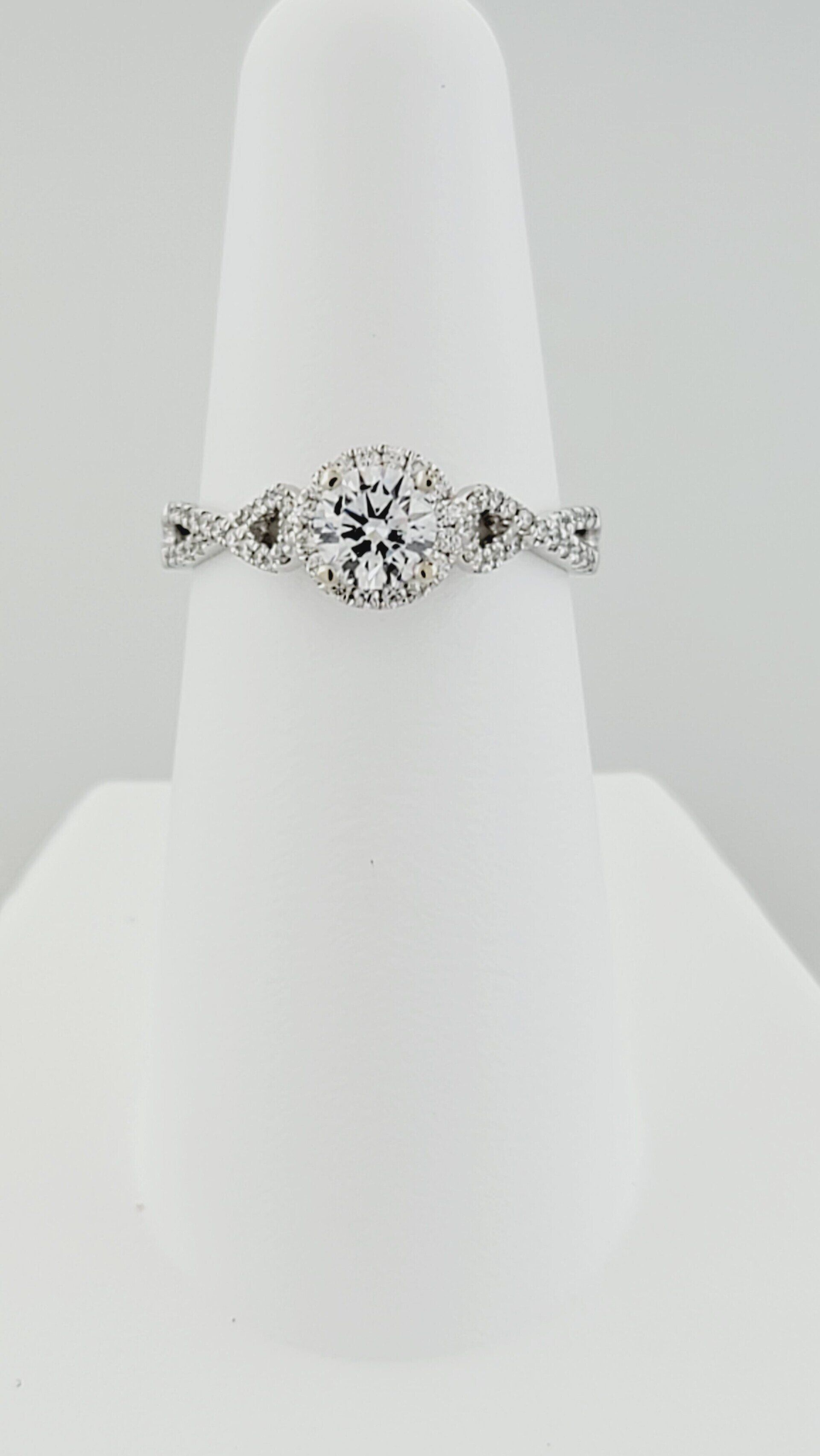 Diamond engagement ring on white display stand.