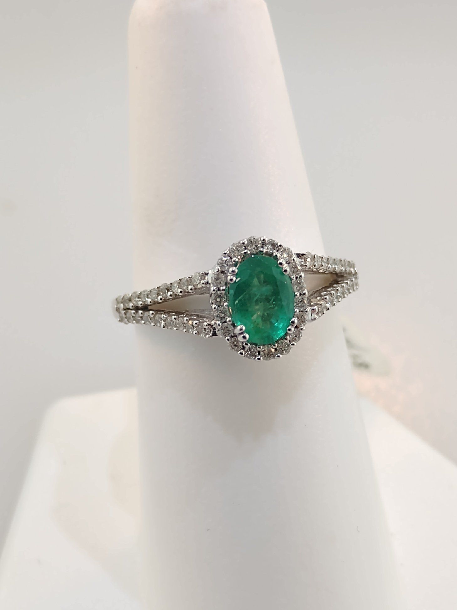 Emerald ring with diamond halo and split shank, displayed on white ring stand.