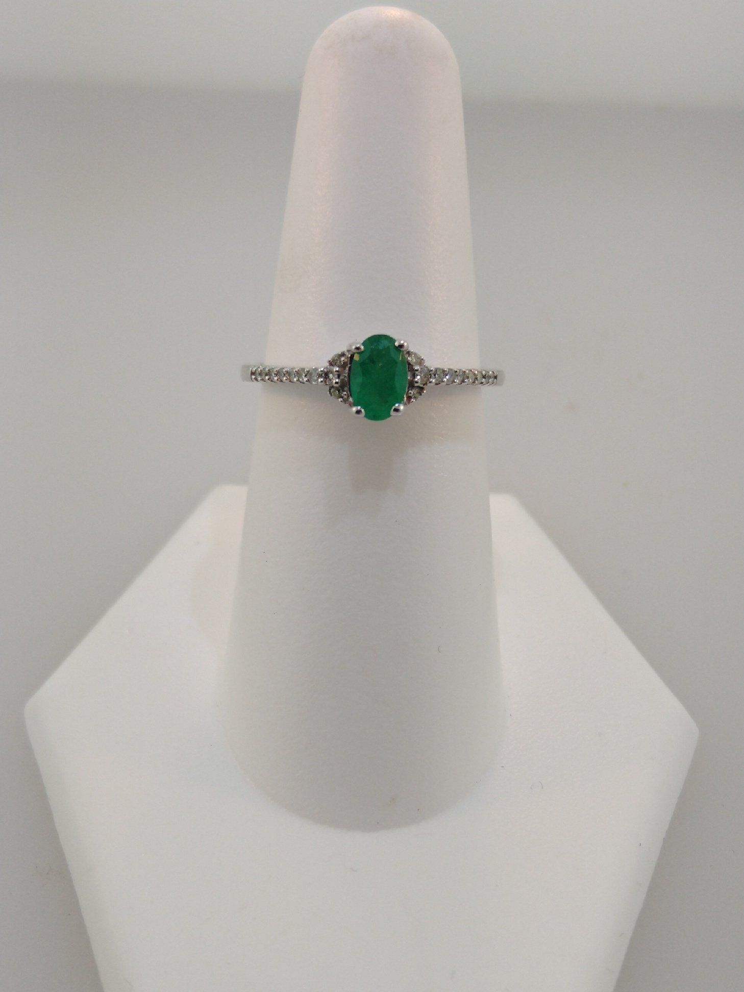 Emerald ring with diamond accents on a white display stand.